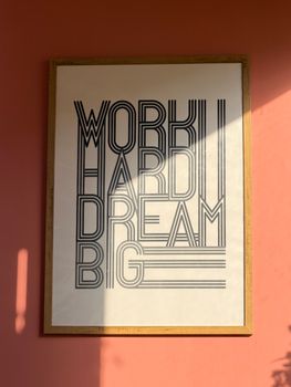 Bold typography on a pink wall inspires with 'Work Hard, Dream Big.' Perfect for motivation.