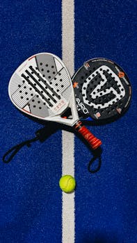 Two padel rackets and a ball placed on a vibrant blue padel court. Bright outdoor shot.