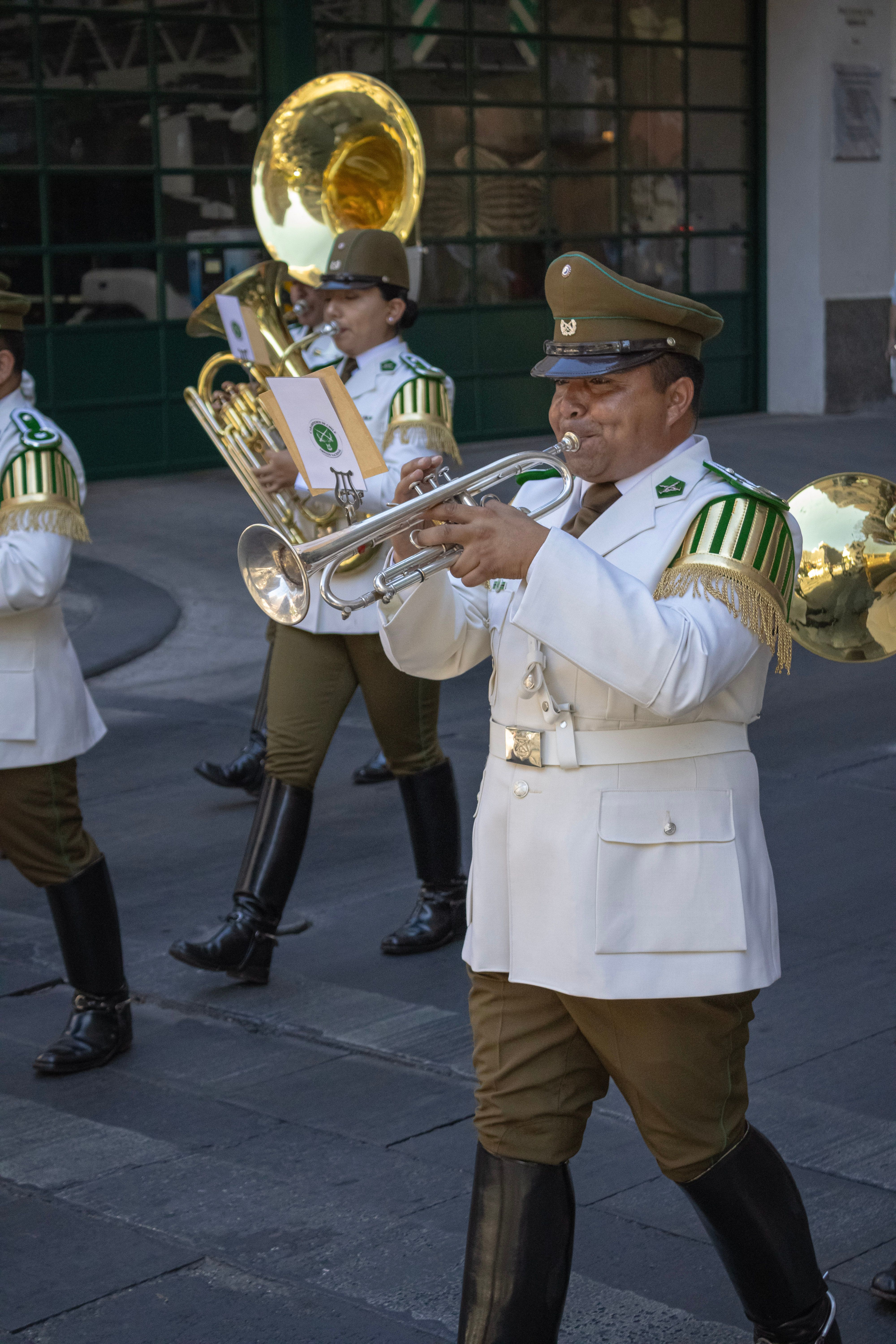 Military band performing in an outdoor parade with brass instruments and full uniforms.