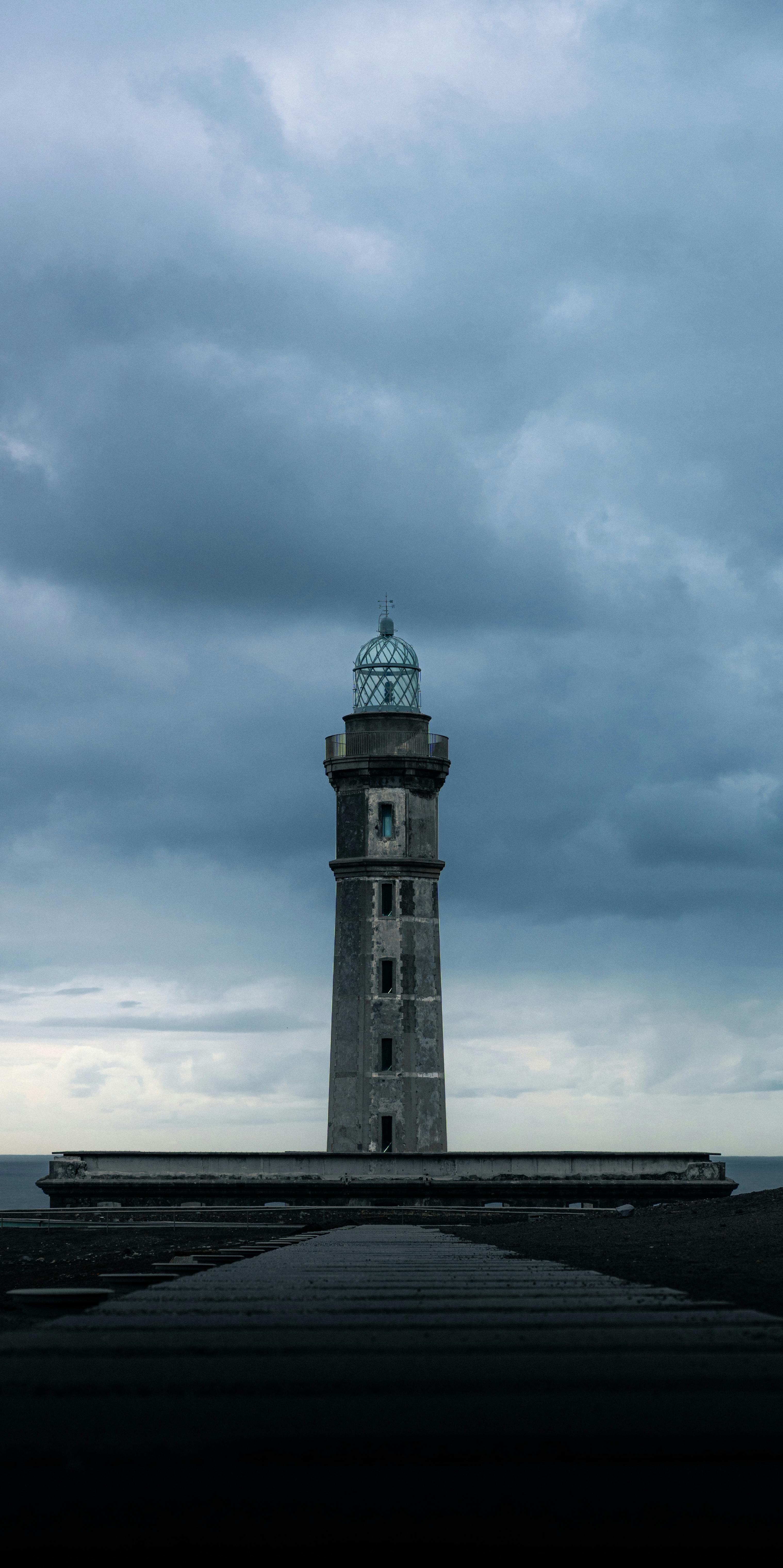 Δωρεάν Ένας μοναχικός φάρος στέκεται επιβλητικός με φόντο σκοτεινά, εντυπωσιακά σύννεφα στη θάλασσα. Φωτογραφία από στοκ φωτογραφιών