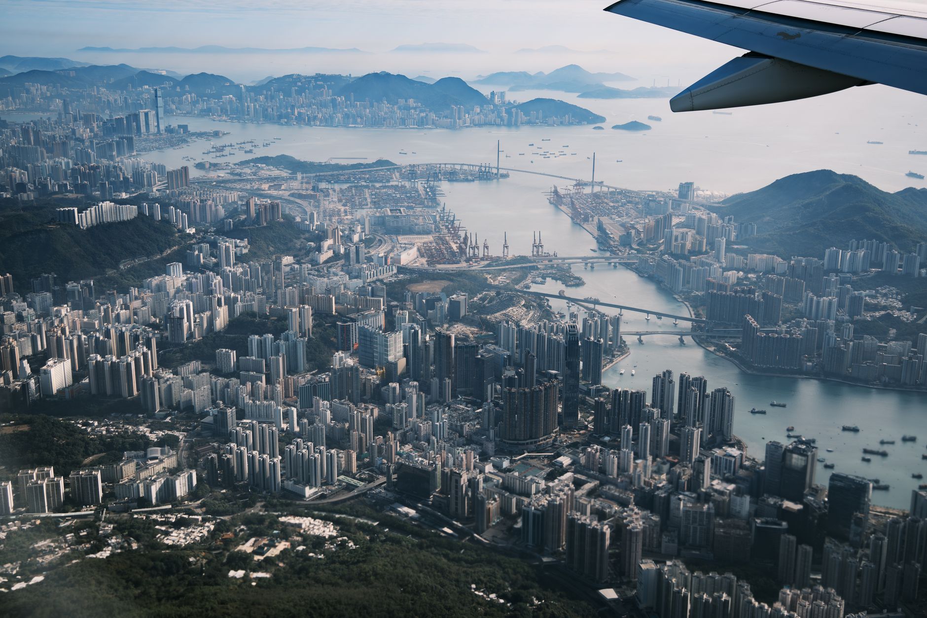 Stunning aerial view of Hong Kong cityscape with mountains and ocean in the background from airplane window.