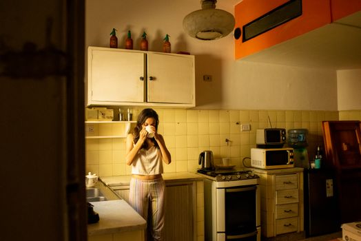 A woman enjoys a warm drink in a vintage style kitchen, capturing a morning moment.