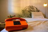 Cozy bedroom with a vintage orange telephone on a white bedspread near a decorative headboard.