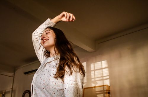 Free A woman in a light blouse joyfully poses indoors with warm, soft lighting creating a serene mood. Stock Photo