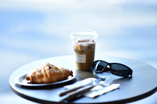 A still life of croissant, iced coffee, and sunglasses on an outdoor table.