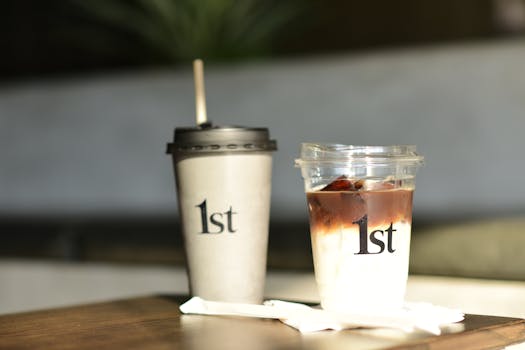 Close-up of latte and iced coffee cups with 1st logo on a wooden table in a modern cafe.