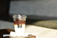 A refreshing iced coffee in a clear cup labeled '1st', sunlight casting warm shadows.