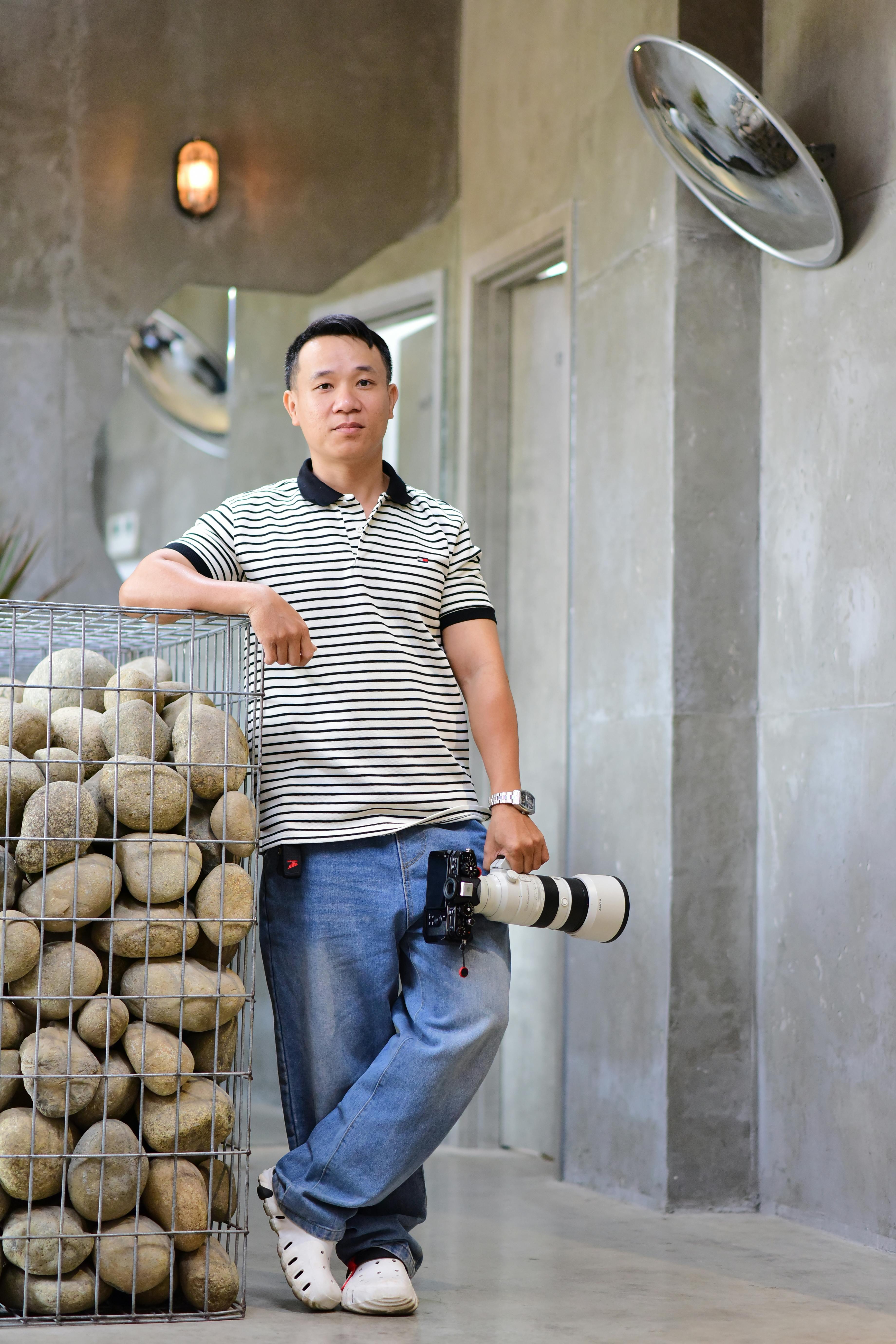 A photographer with a large lens posing indoors by a rock display.