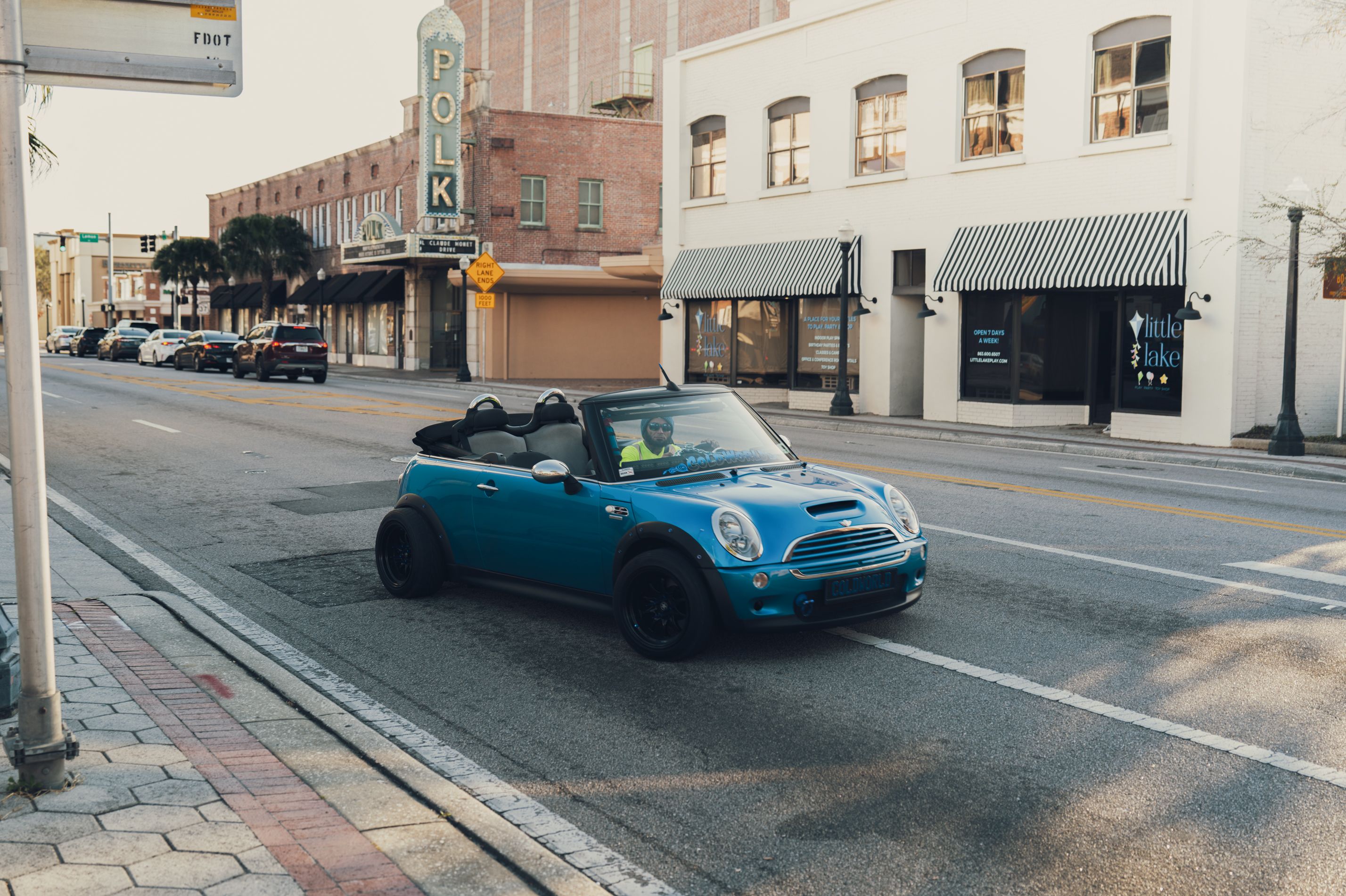 A blue convertible driving on a downtown street with historic buildings in the background.