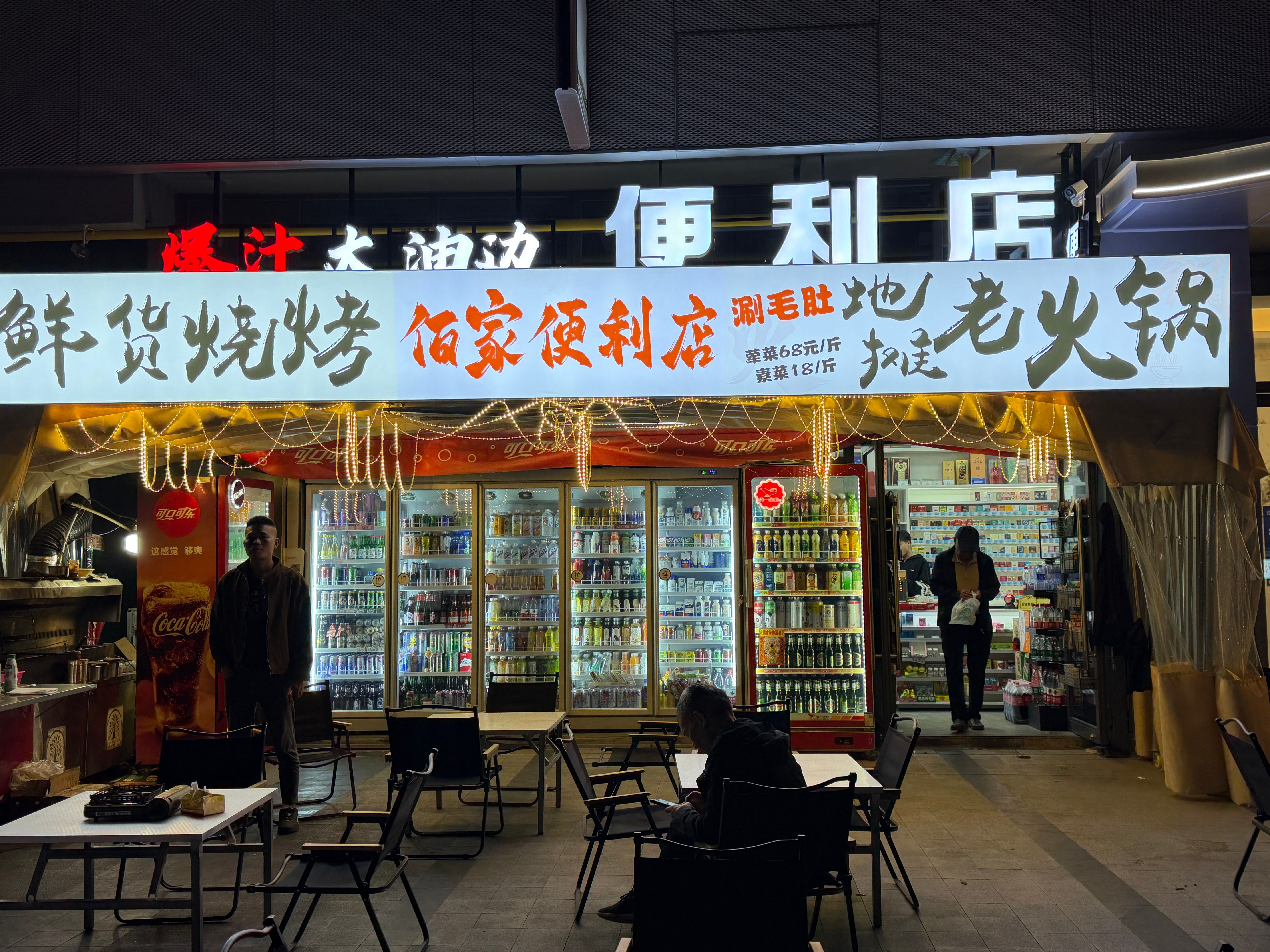 Illuminated convenience store at night with people shopping and eating outside.