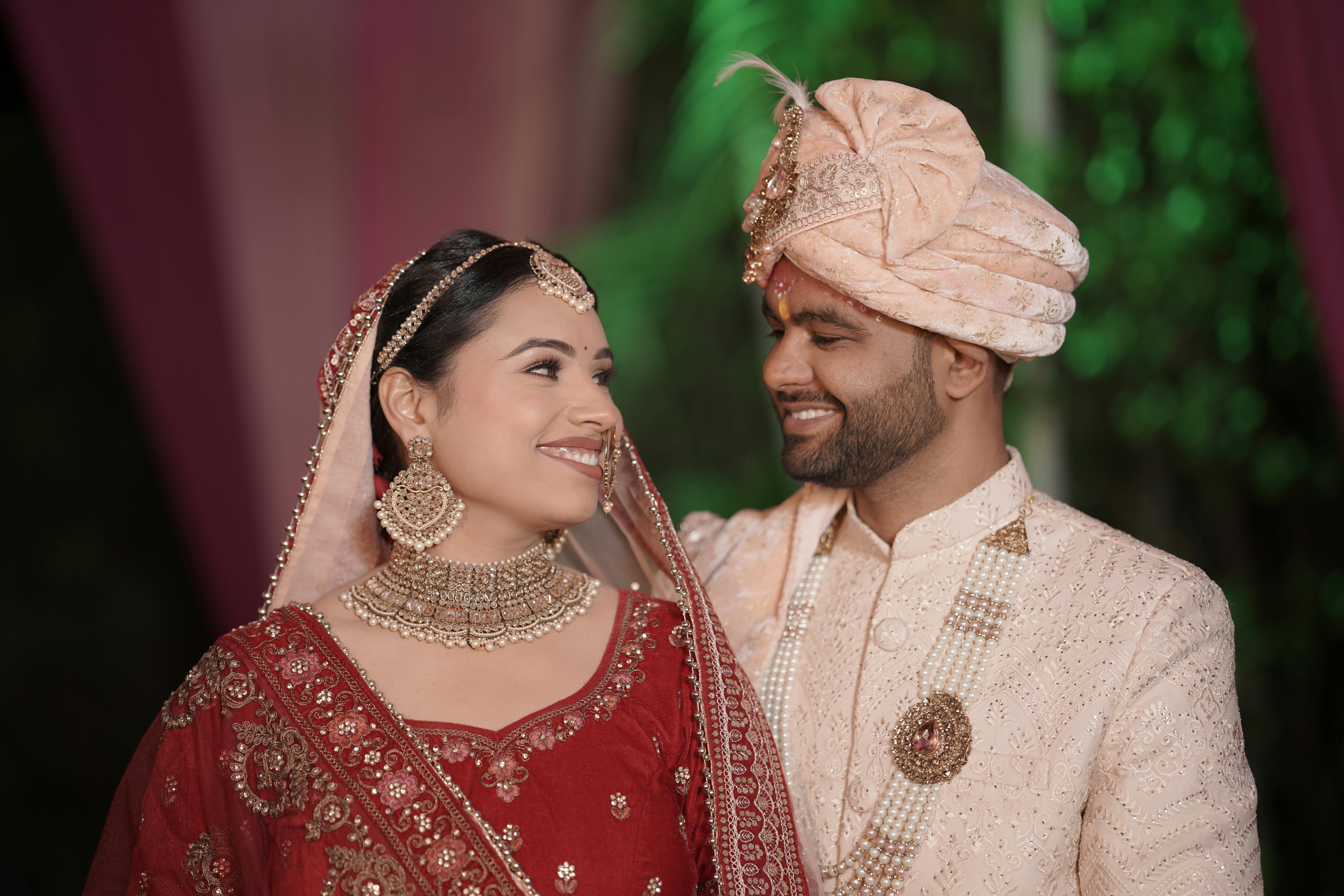 A joyful Indian couple in traditional wedding attire, adorned with intricate embroidery and jewelry.