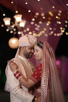 A joyful Indian couple in traditional wedding attire, captured in an intimate moment under decorative lights.