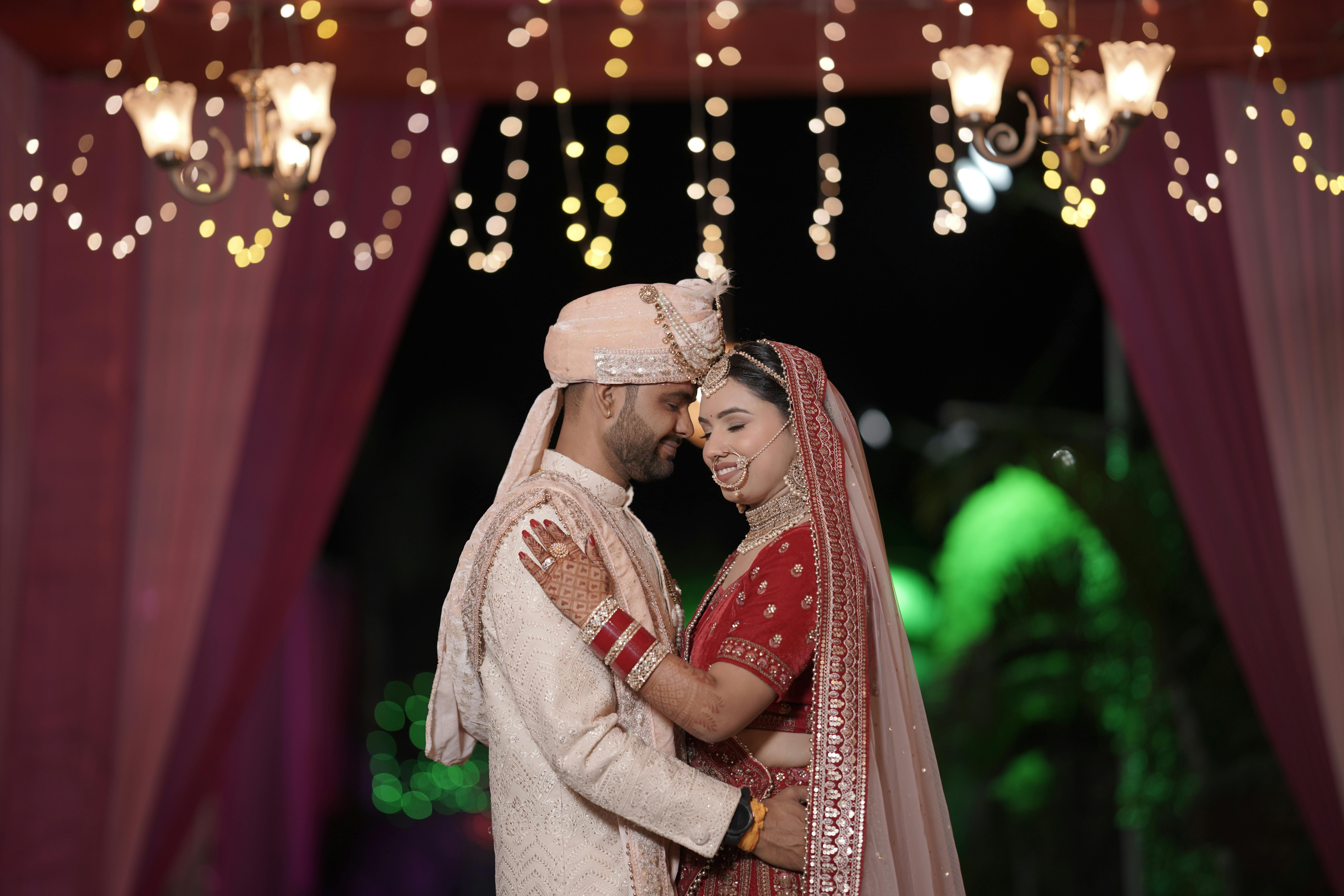An Indian couple in traditional attire sharing a tender moment under illuminated decorations.