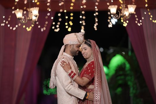 An Indian couple in traditional attire sharing a tender moment under illuminated decorations.