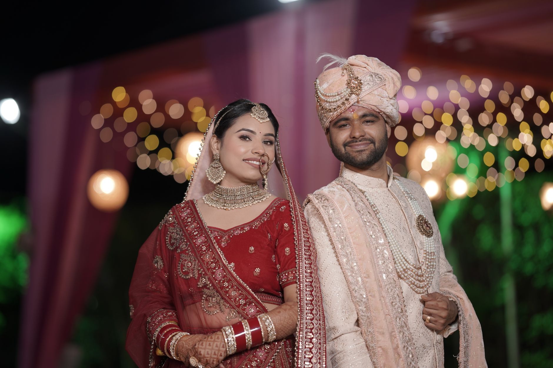 Happy Indian bride and groom in traditional attire at their wedding ceremony with festive background lighting.