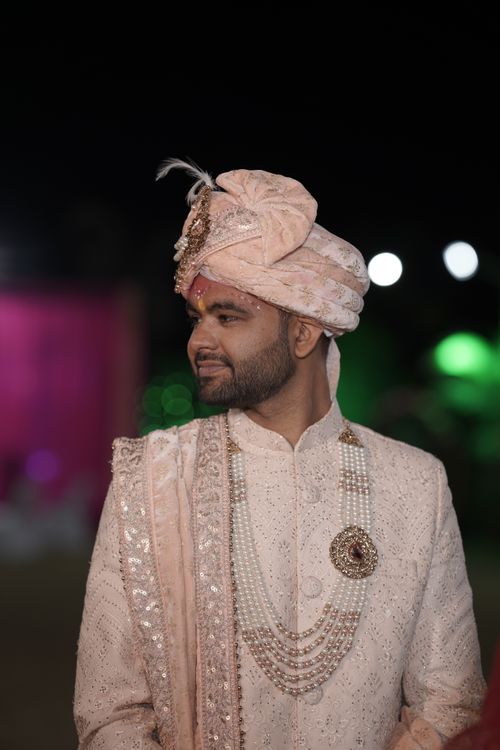 Free A South Asian groom elegantly dressed in traditional attire with intricate embroidery and jewelry, smiling during a night wedding ceremony. Stock Photo