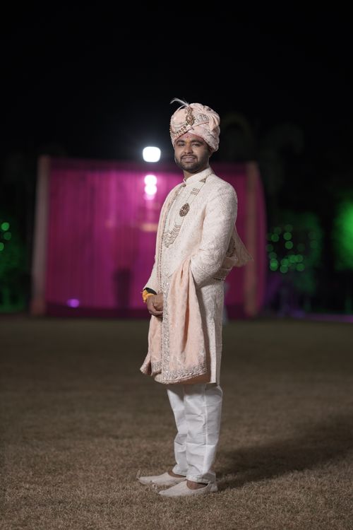 Free A groom in a traditional sherwani standing outdoors at night during a ceremonial event. Stock Photo