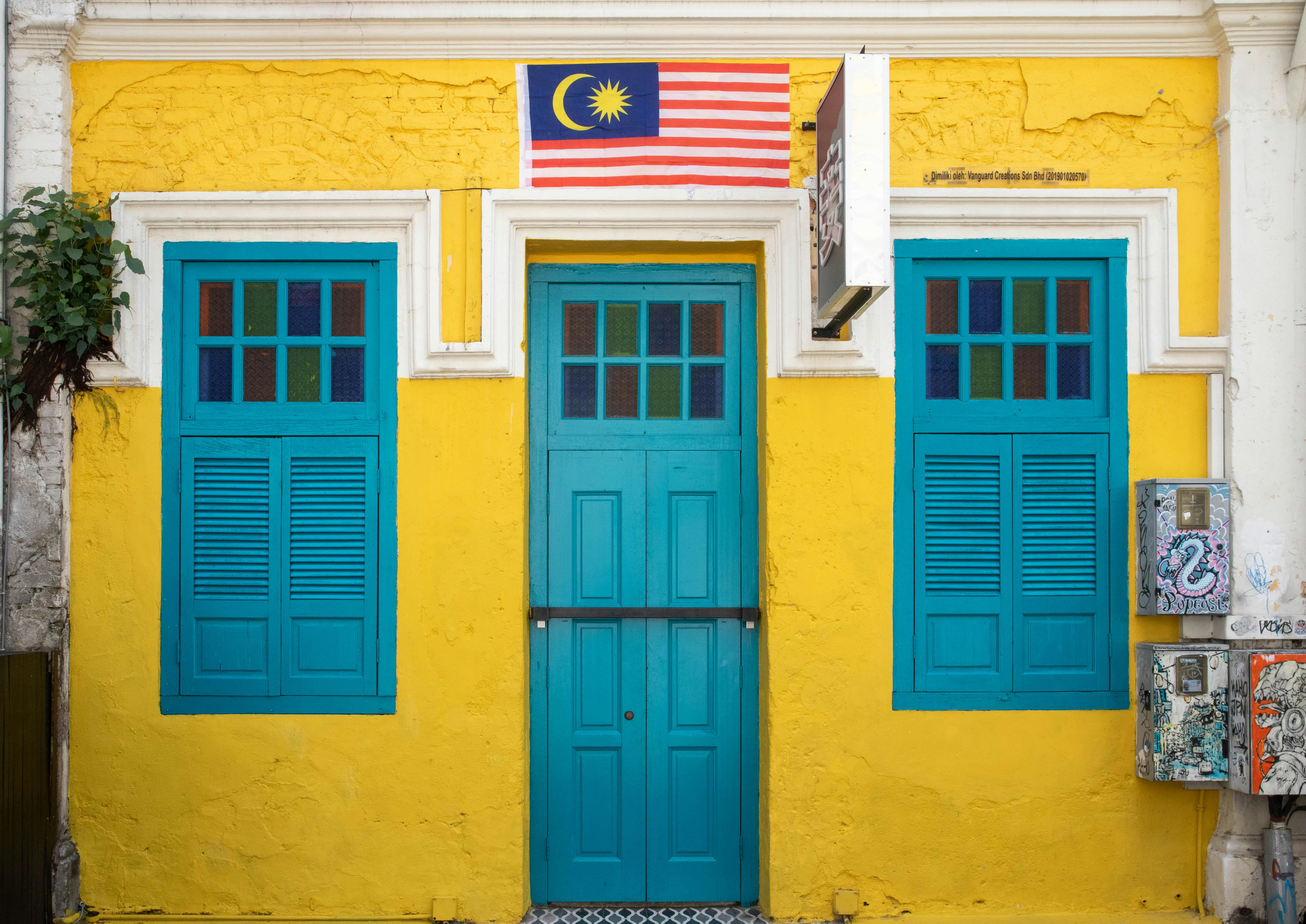 Kostenlos Leuchtend gelbe und türkisfarbene Fassade mit malaysischer Flagge. Lebendige Architektur und kulturelles Symbol. Stock-Foto