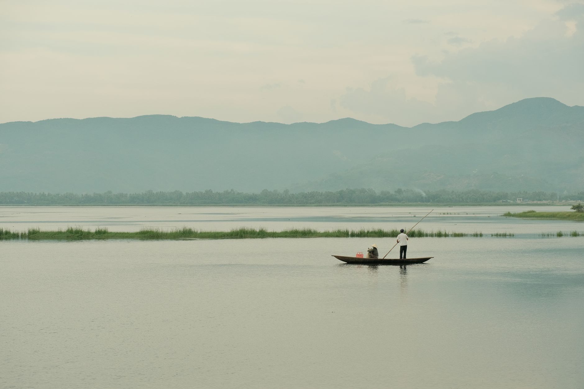 Two people fishing on a calm lake in Vietnam with mountains in the background.