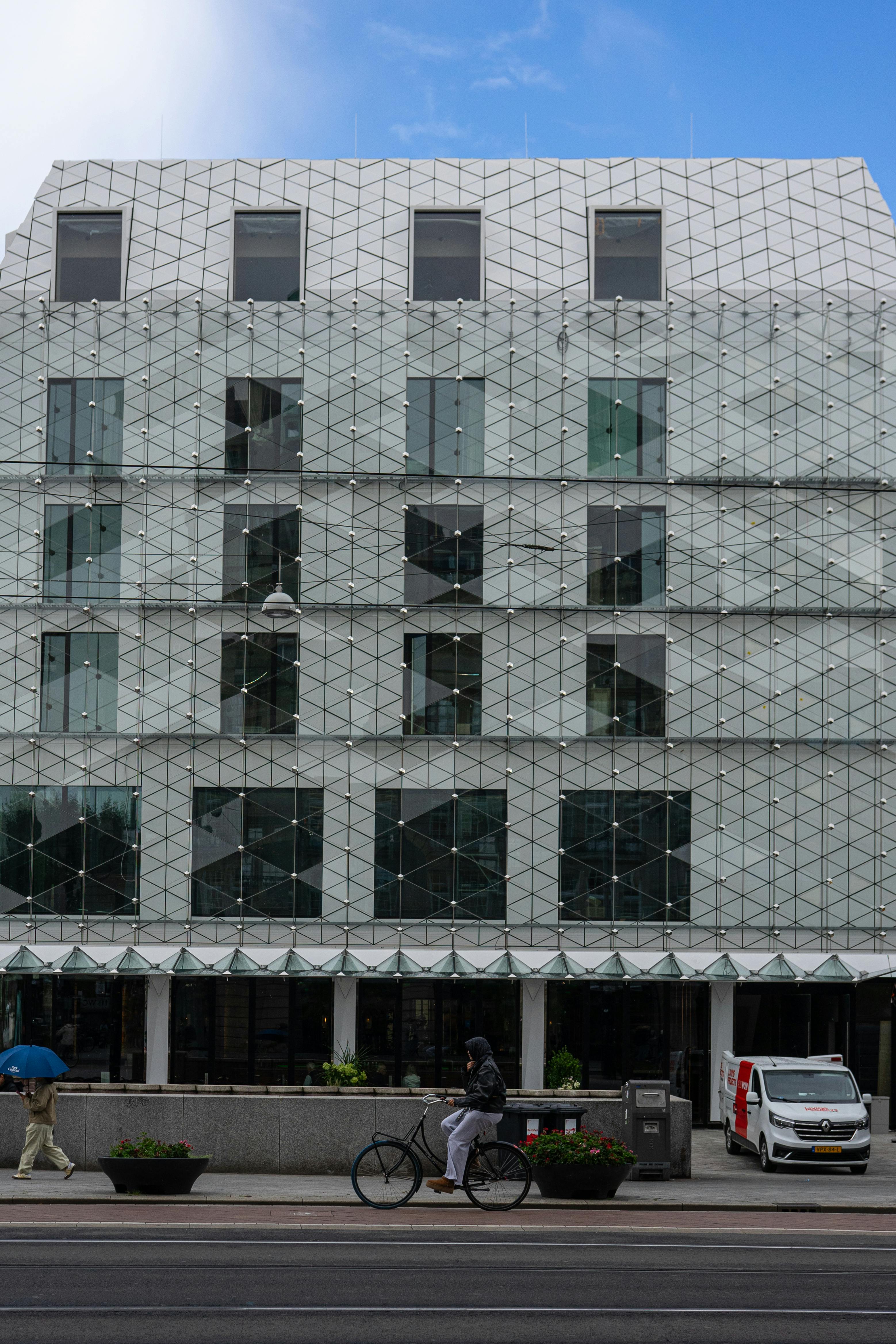 Δωρεάν Σύγχρονη πρόσοψη κτιρίου στο Άμστερνταμ με ποδηλάτη και πεζό σε μια καθαρή μέρα. Φωτογραφία από στοκ φωτογραφιών