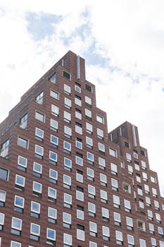 Low angle view of a modern brick building in Amsterdam against a cloudy sky.