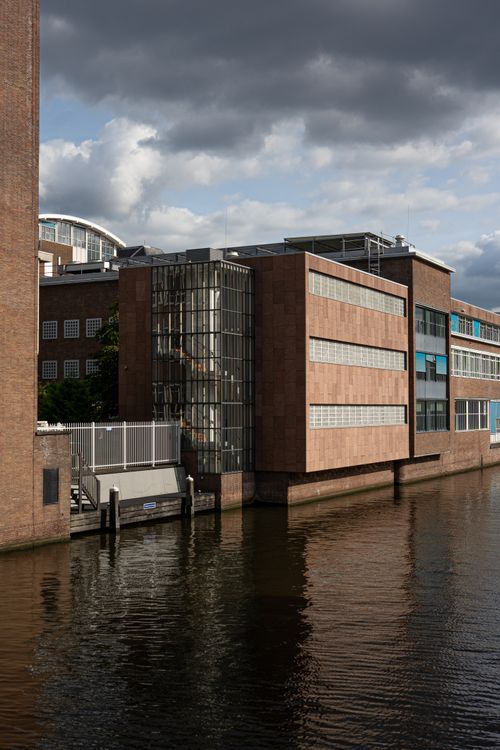Free A modern architectural building by a canal in Amsterdam under a cloudy sky. Stock Photo