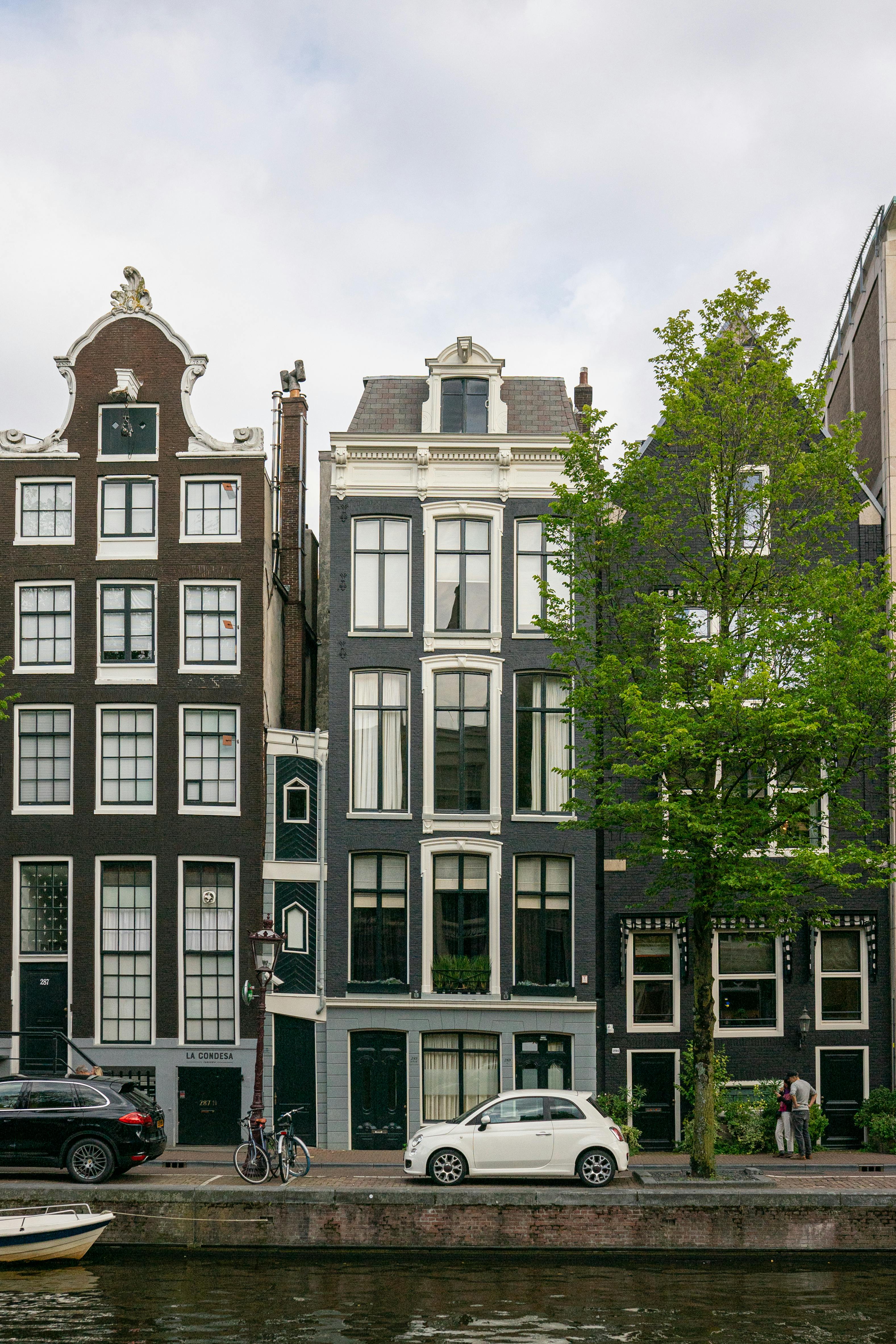 Δωρεάν Κλασικά σπίτια δίπλα σε κανάλια στο Άμστερνταμ με ποδήλατα και αυτοκίνητα παραταγμένα κατά μήκος του δρόμου. Φωτογραφία από στοκ φωτογραφιών