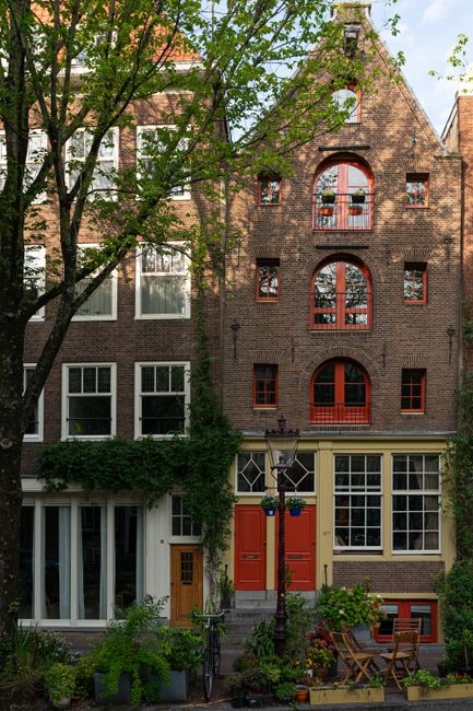 Charming Amsterdam canal houses with red accents and lush greenery.