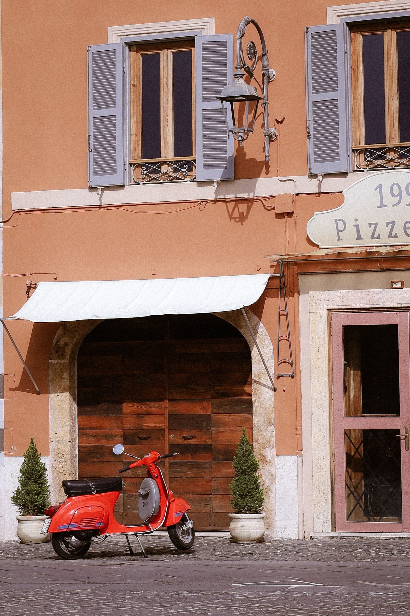 Vintage red Vespa parked outside an Italian pizzeria in a charming street setting.