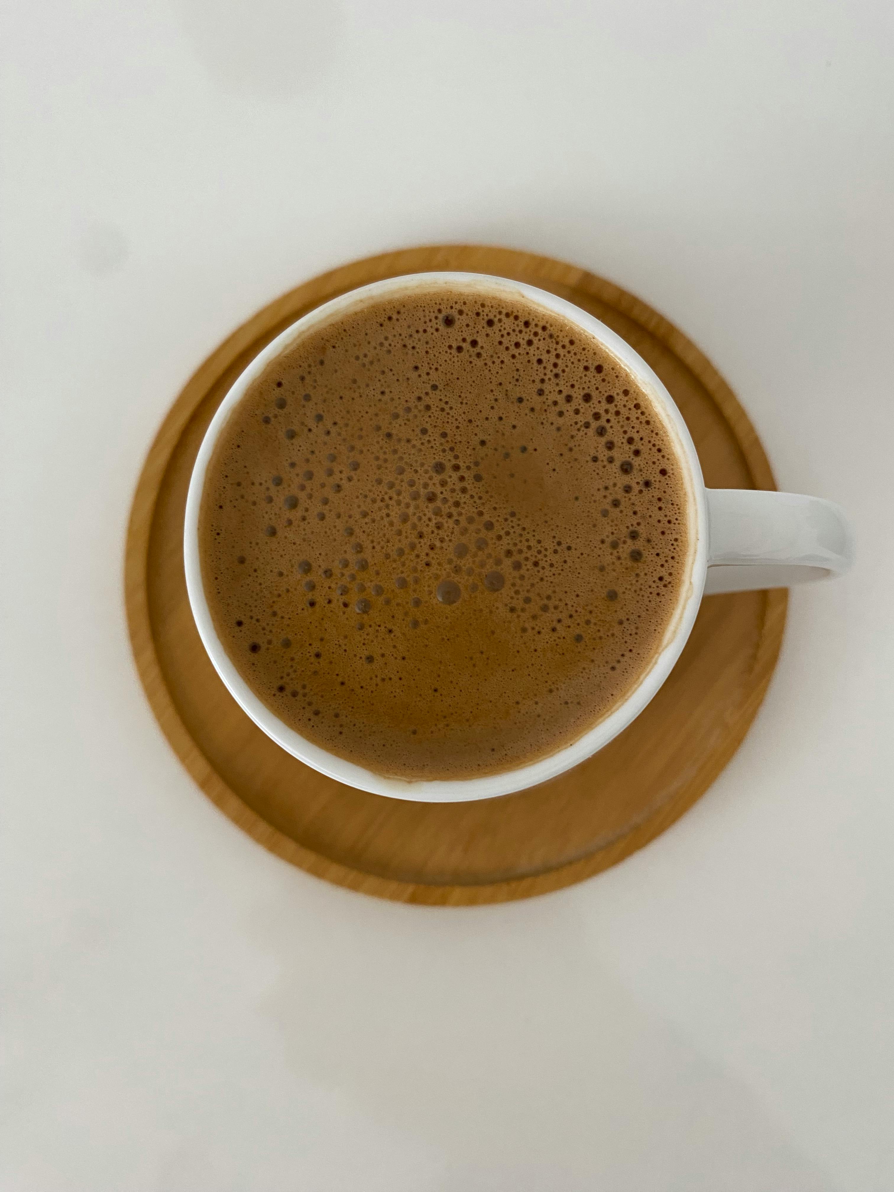 Δωρεάν Άποψη από πάνω προς τα κάτω αφρώδους καφέ σε μια λευκή κούπα σε ένα ξύλινο σουβέρ, δημιουργώντας μια ζεστή ατμόσφαιρα. Φωτογραφία από στοκ φωτογραφιών