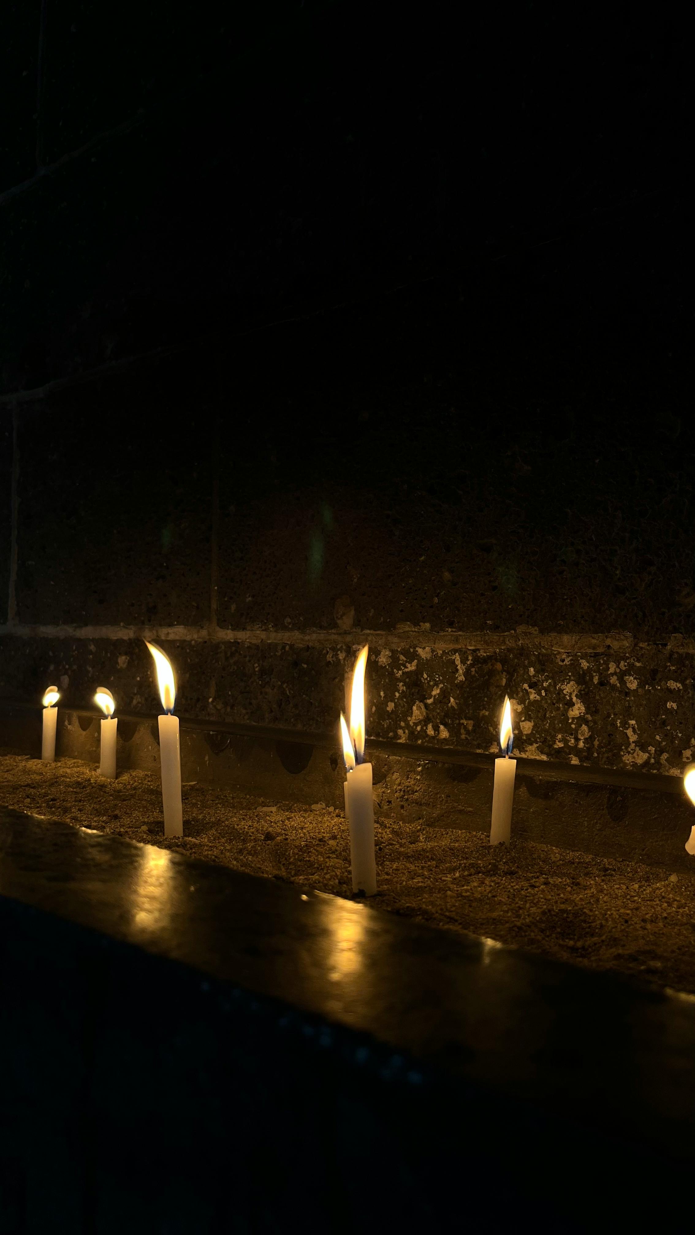 Free A row of lit candles casting a warm glow in a dark, serene space. Stock Photo