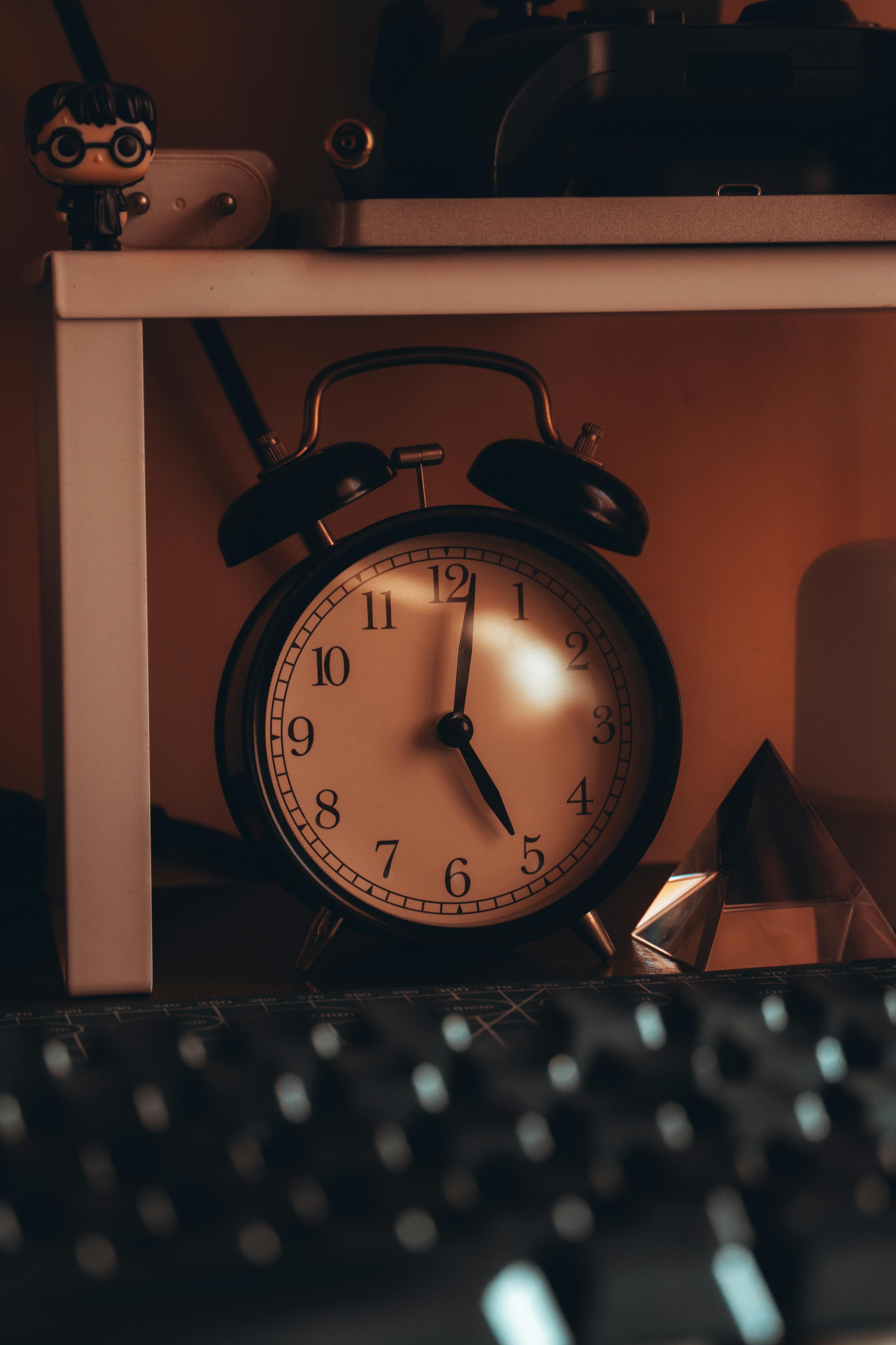 Free An antique alarm clock on a cozy bedside table casting artistic shadows with warm lighting. Stock Photo