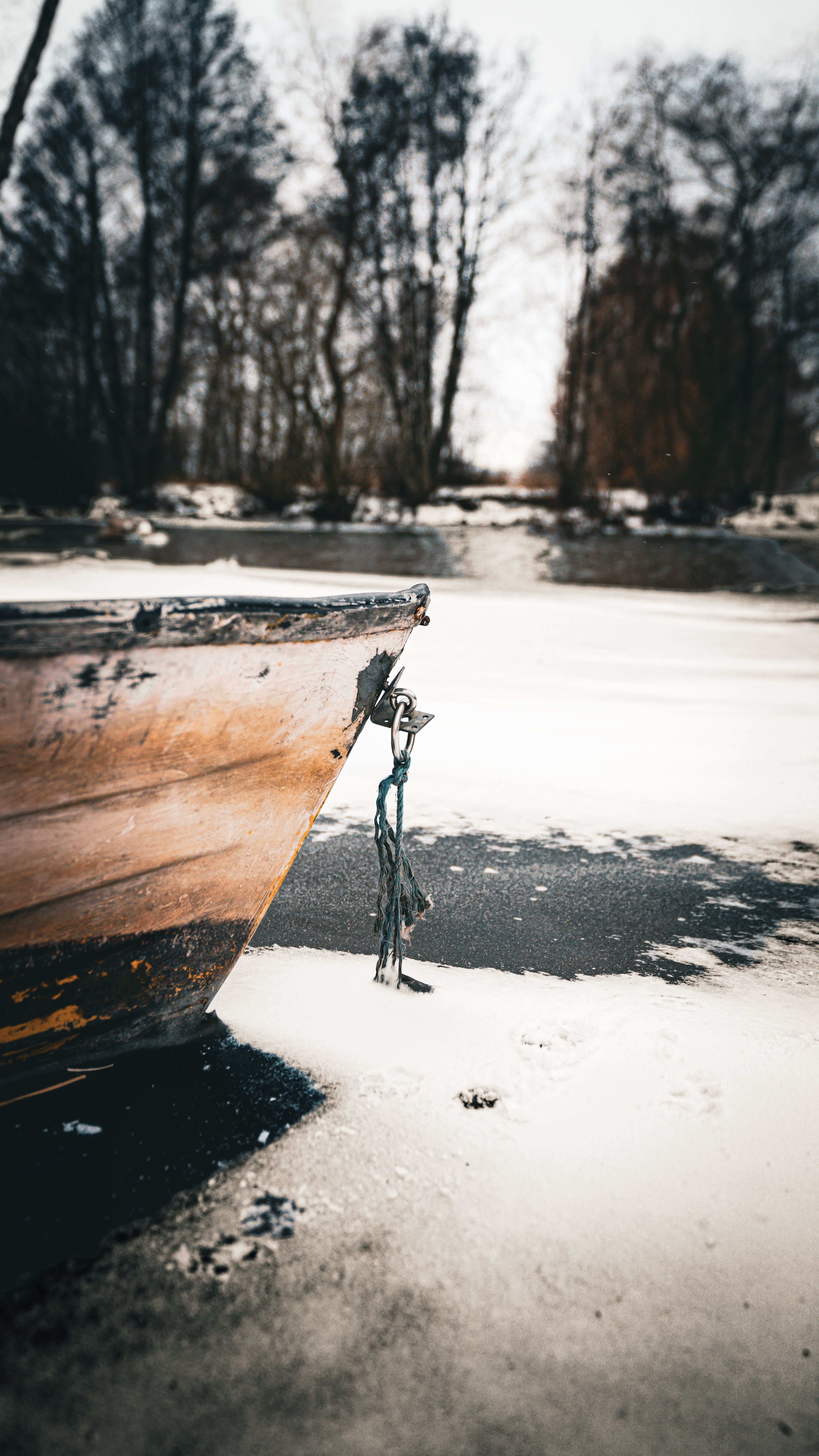 Wooden boat at a snowy frozen lakeside, surrounded by bare trees in winter.