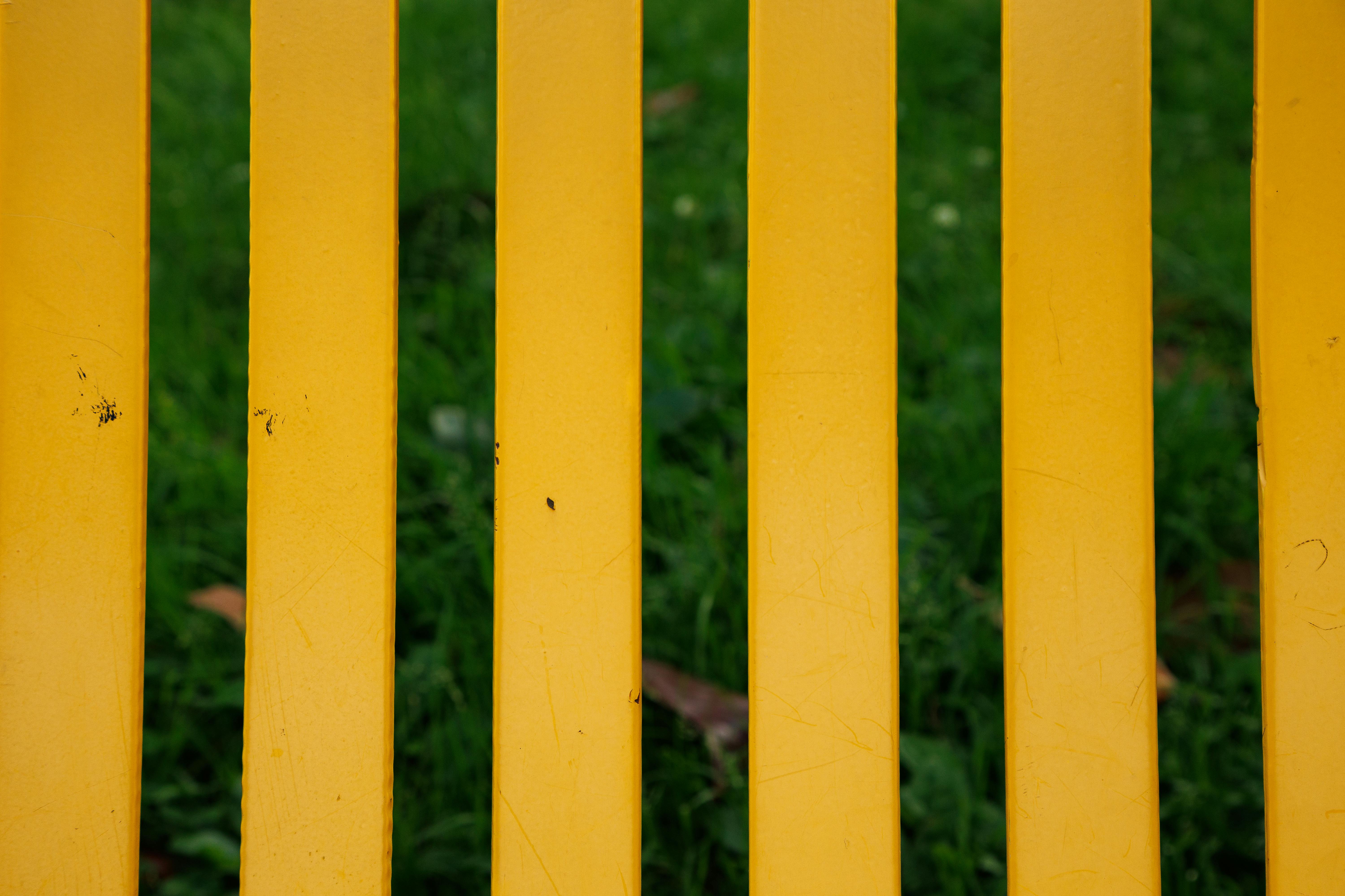 Free Close-up of a yellow fence with green grass in the background, capturing bold colors and texture. Stock Photo