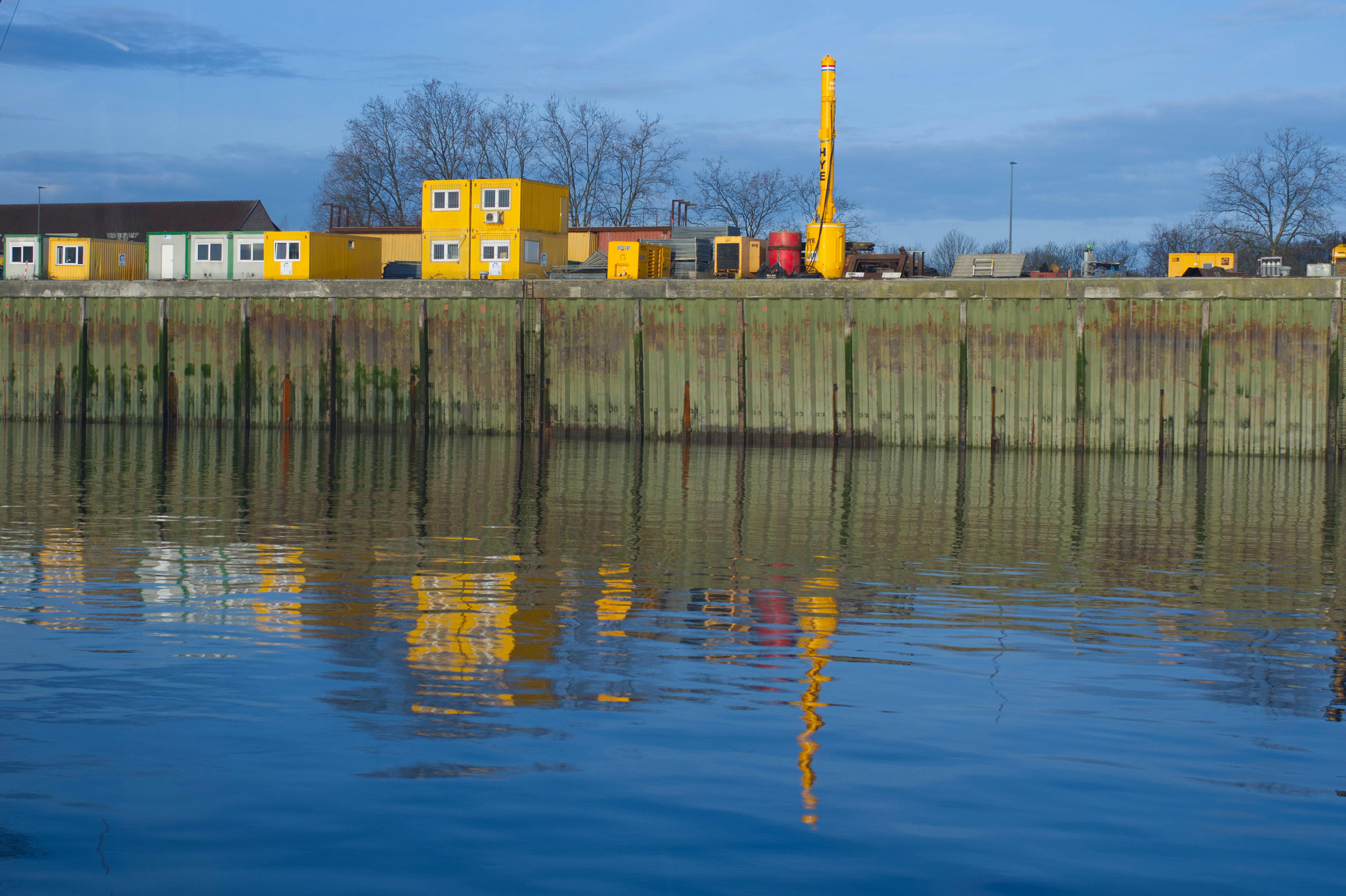 Kostenlos Lebendige Industrieszene mit gelben Containern am Wasser unter klarem Himmel. Stock-Foto