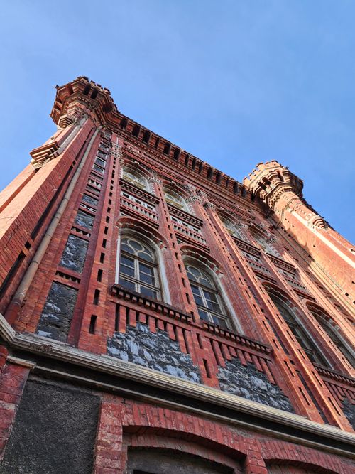 Free Upward view of historic red brick building with ornate architecture against a clear blue sky. Stock Photo