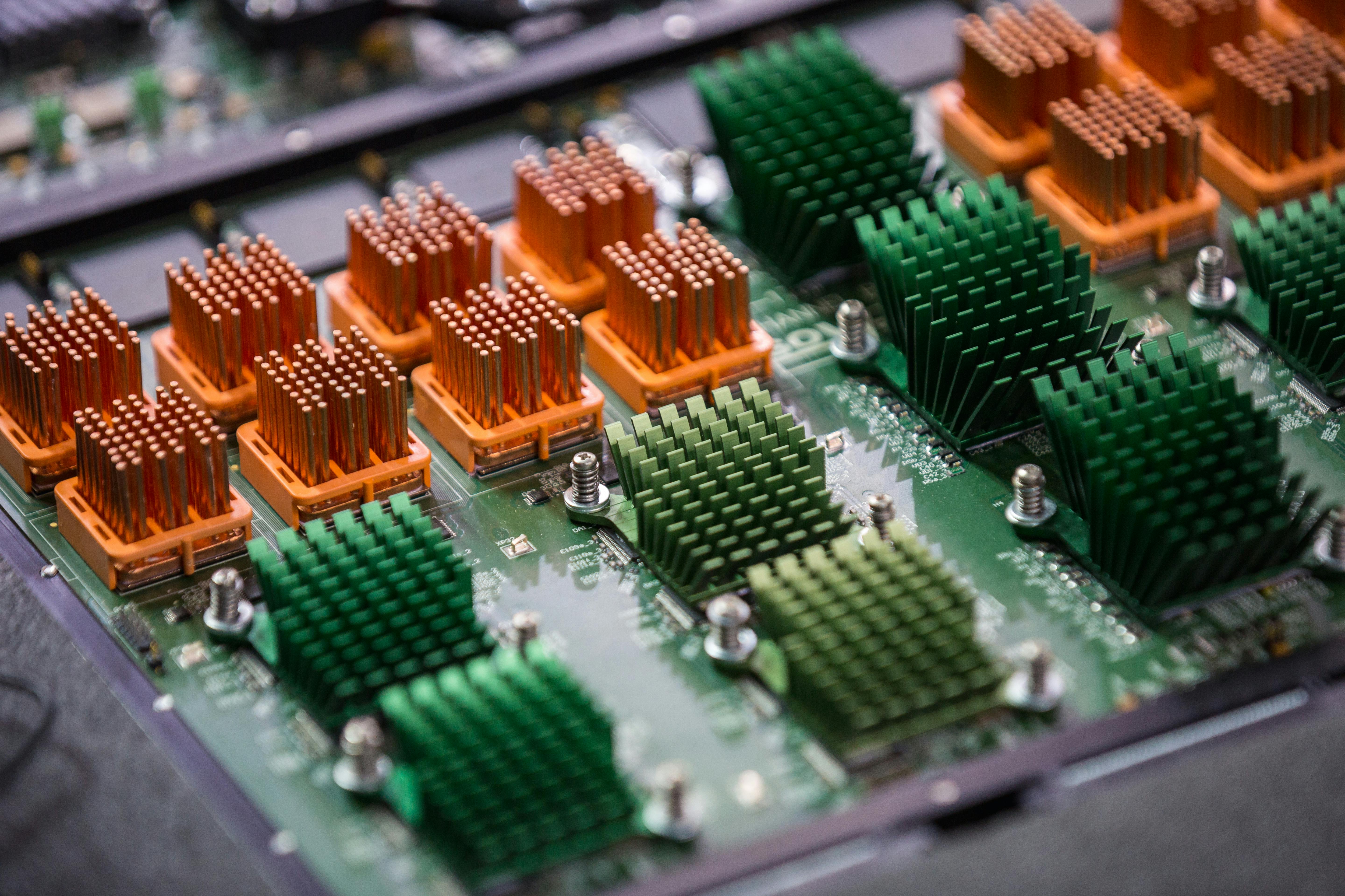 Kostenlos Detailansicht einer Computerplatine mit orangefarbenen und grünen Kühlkörpern, die die Technologiekomponenten hervorhebt. Stock-Foto