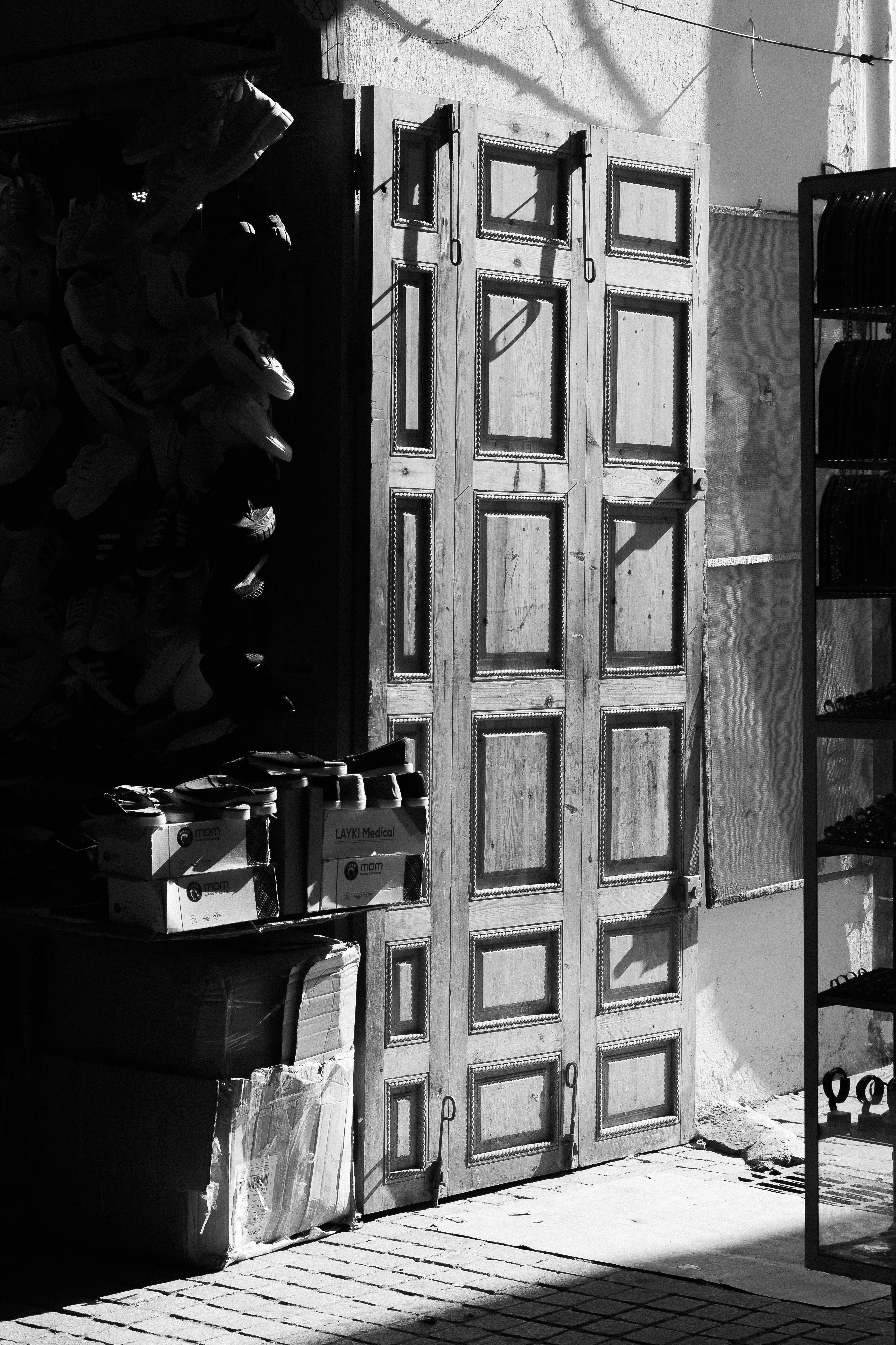 Free Black and white image of rustic wooden doors with dramatic shadows in an urban alleyway. Stock Photo
