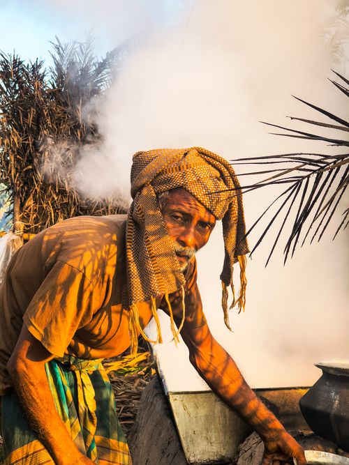 Free Elderly man involved in traditional sugar production with natural surroundings and steam. Stock Photo