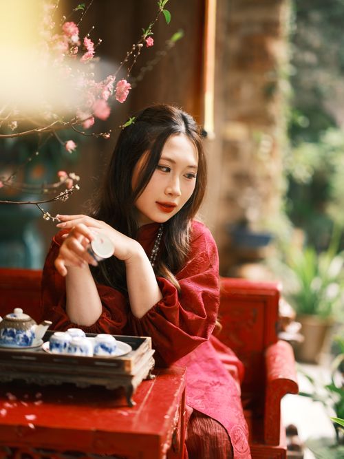 Free Elegant woman in red enjoying tea with blossoming flowers in a serene garden ambiance. Stock Photo