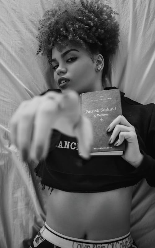 Monochrome Photo of Woman Lying on Bed While Holding a Book