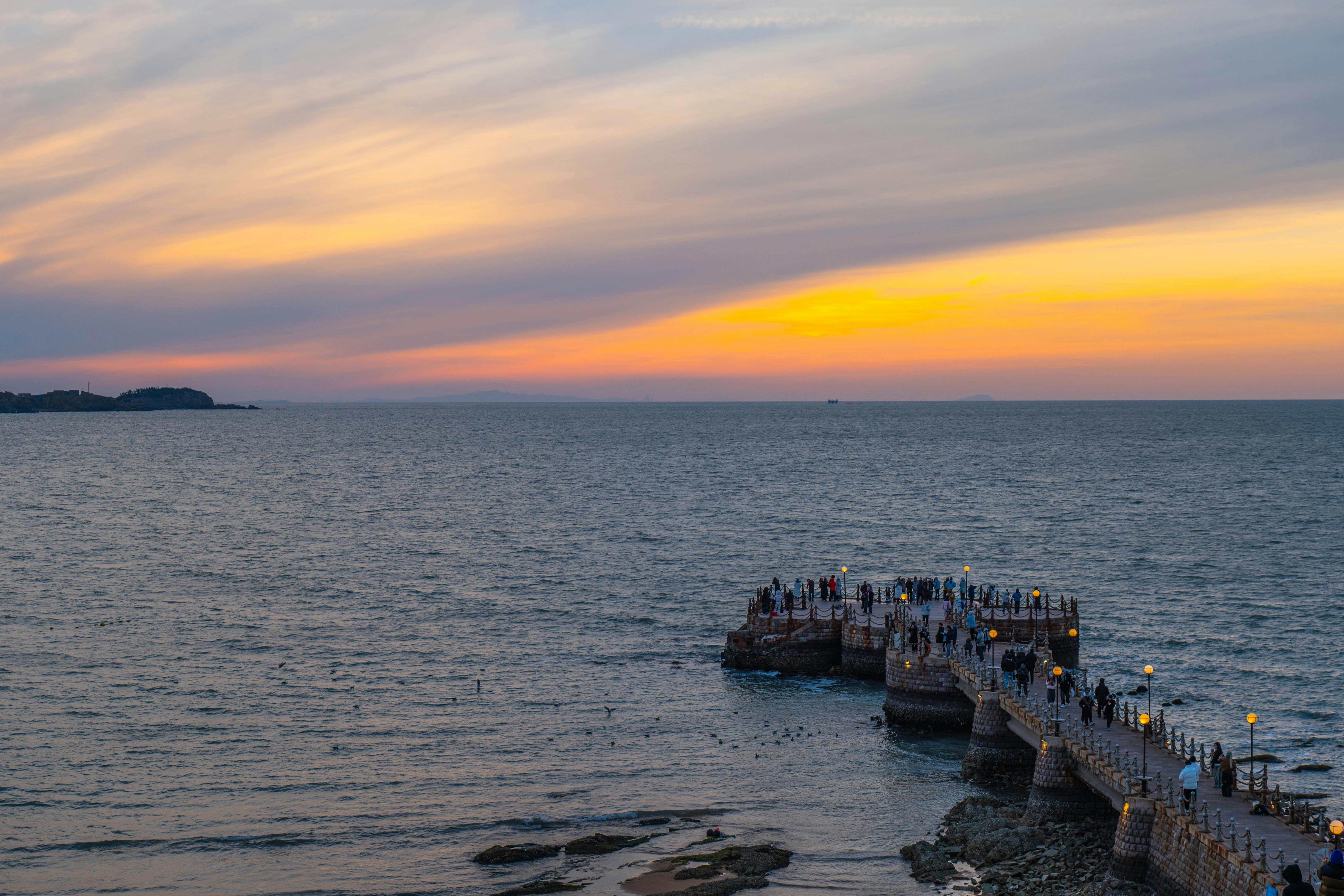 A serene sunset over an ocean pier with people enjoying the view.