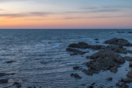 Free Peaceful ocean sunset scene with rocky coastline, perfect for travel or nature themes. Stock Photo