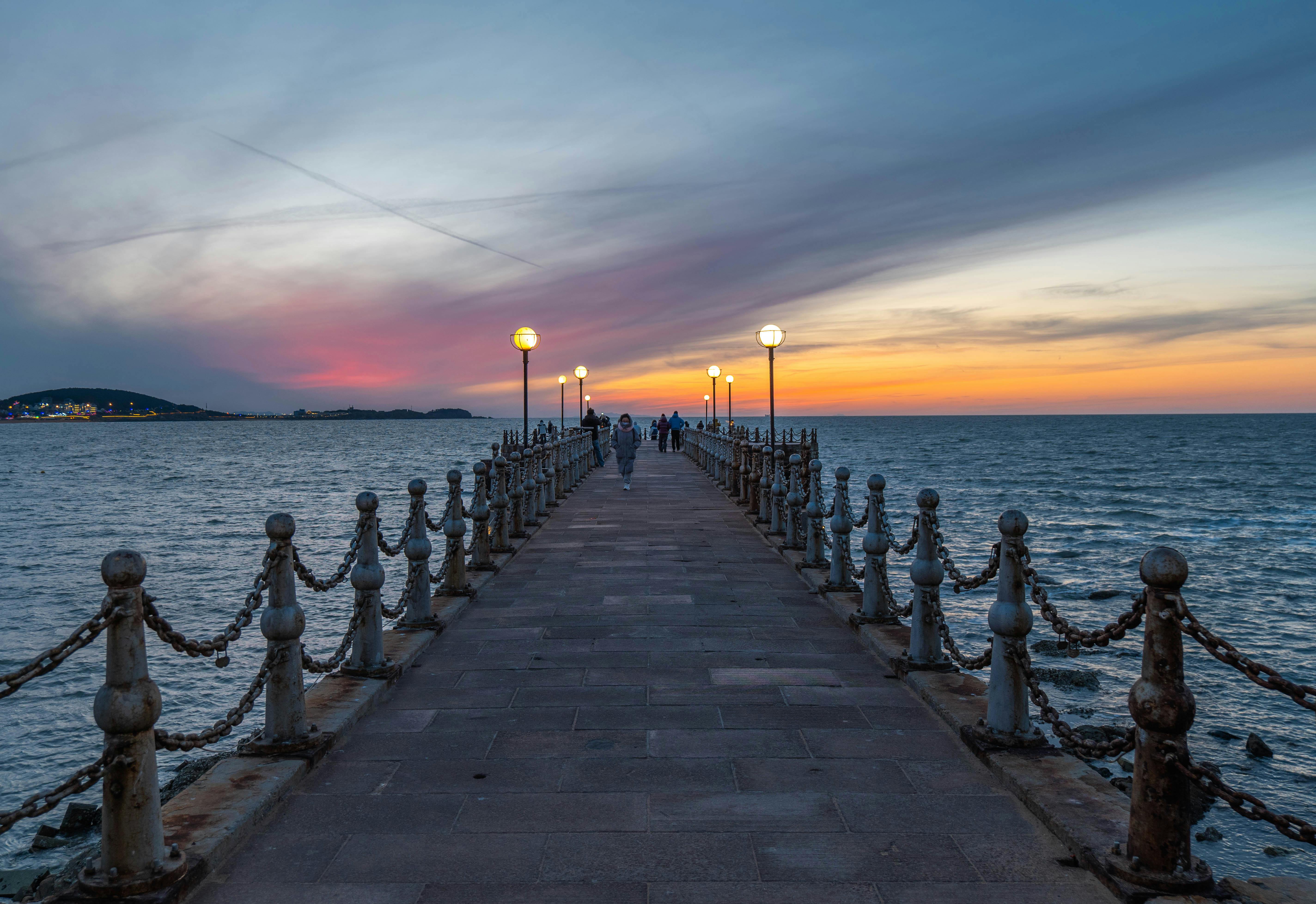 Gratis En fantastisk solnedgang over en brygge ved sjøen med gatelykter og en fargerik himmel. Arkivbilde