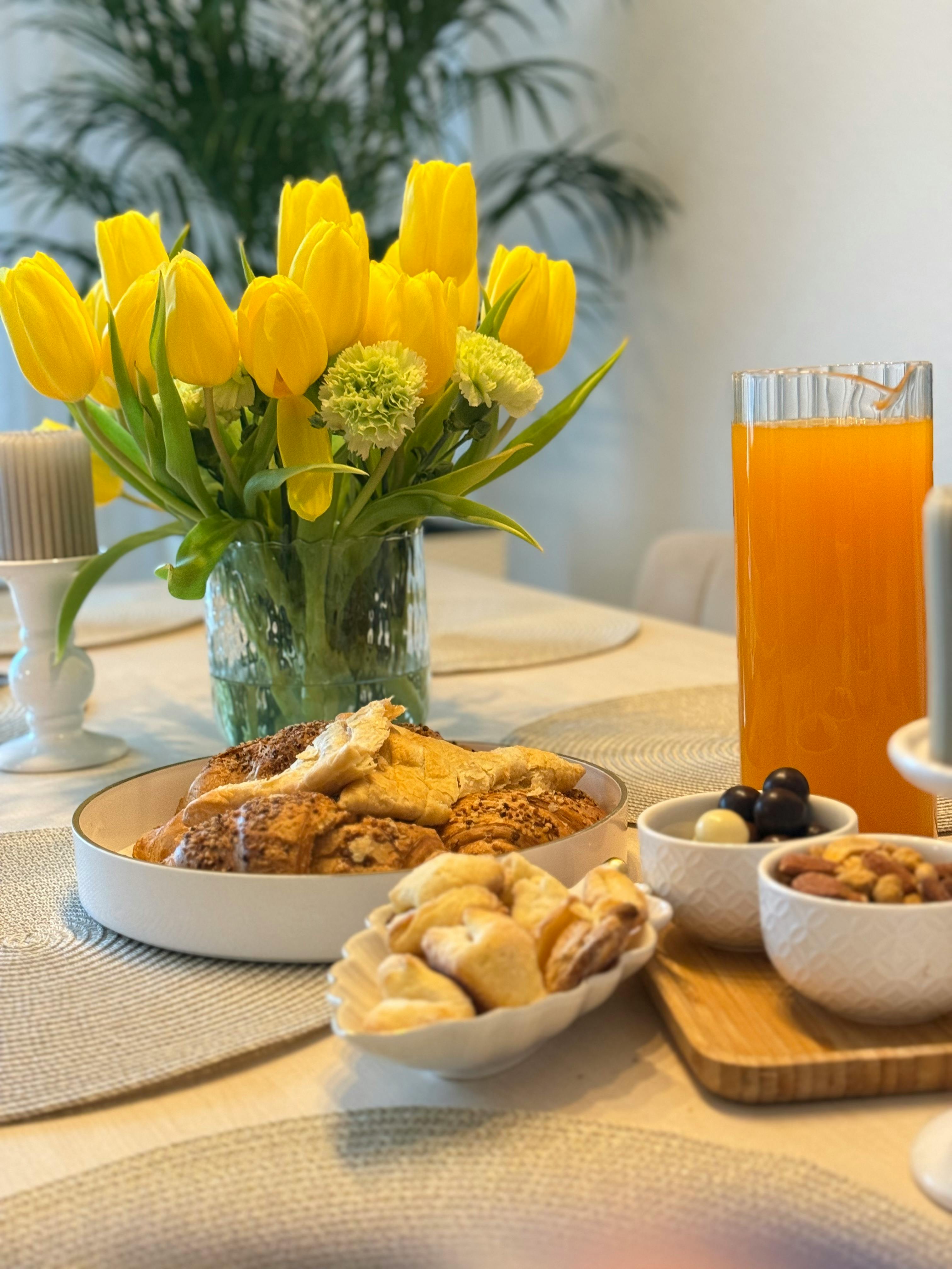 Gratis Indbydende forårsbrunch med gule tulipaner, kager og appelsinjuice i hyggelige omgivelser. Lagerfoto