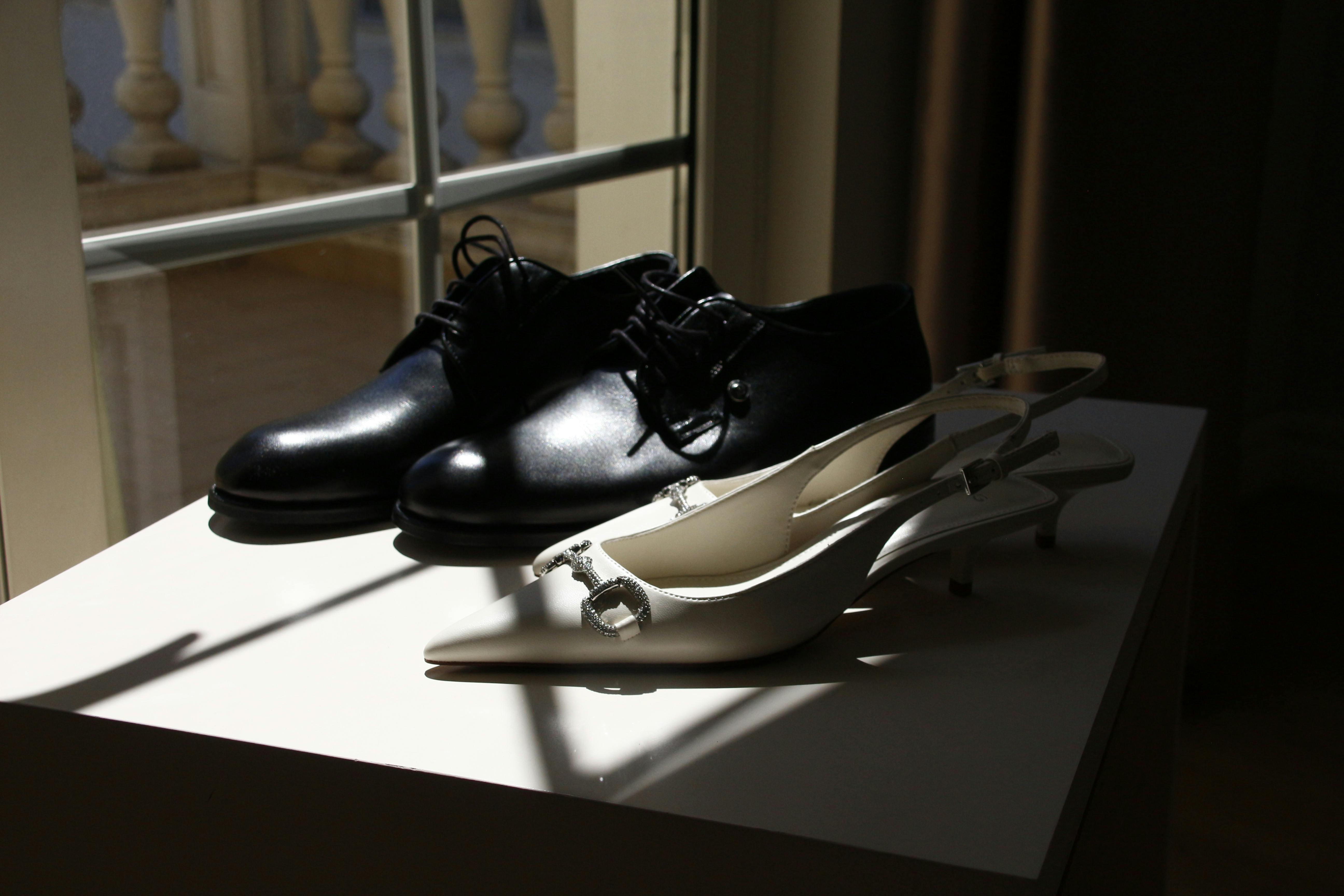 Close-up of stylish black men's and white women's shoes in sunlight by a window.