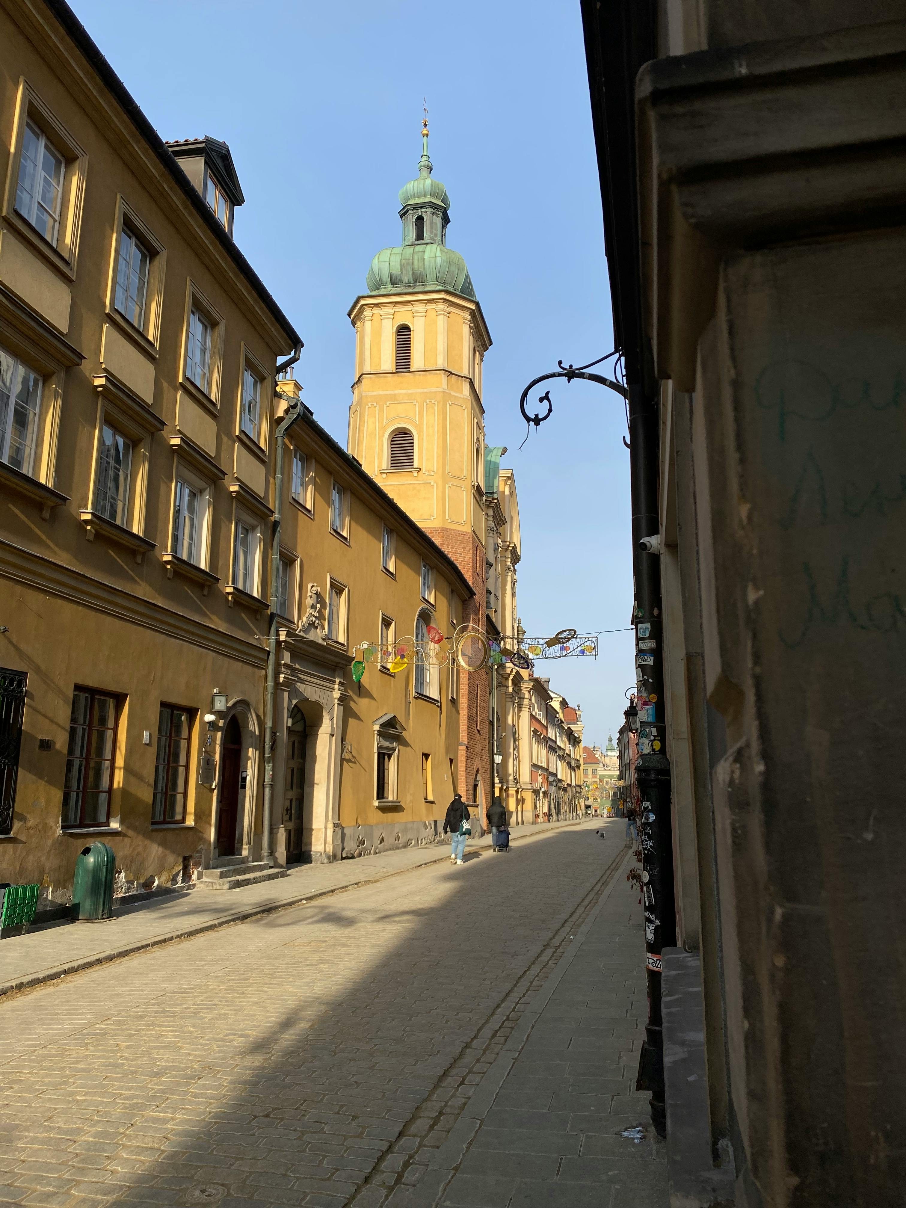 Δωρεάν Ένας γραφικός δρόμος στην παλιά πόλη της Βαρσοβίας, με ιστορική αρχιτεκτονική και ένα περίφημο καμπαναριό, απαθανατισμένος κατά τη διάρκεια της ημέρας. Φωτογραφία από στοκ φωτογραφιών