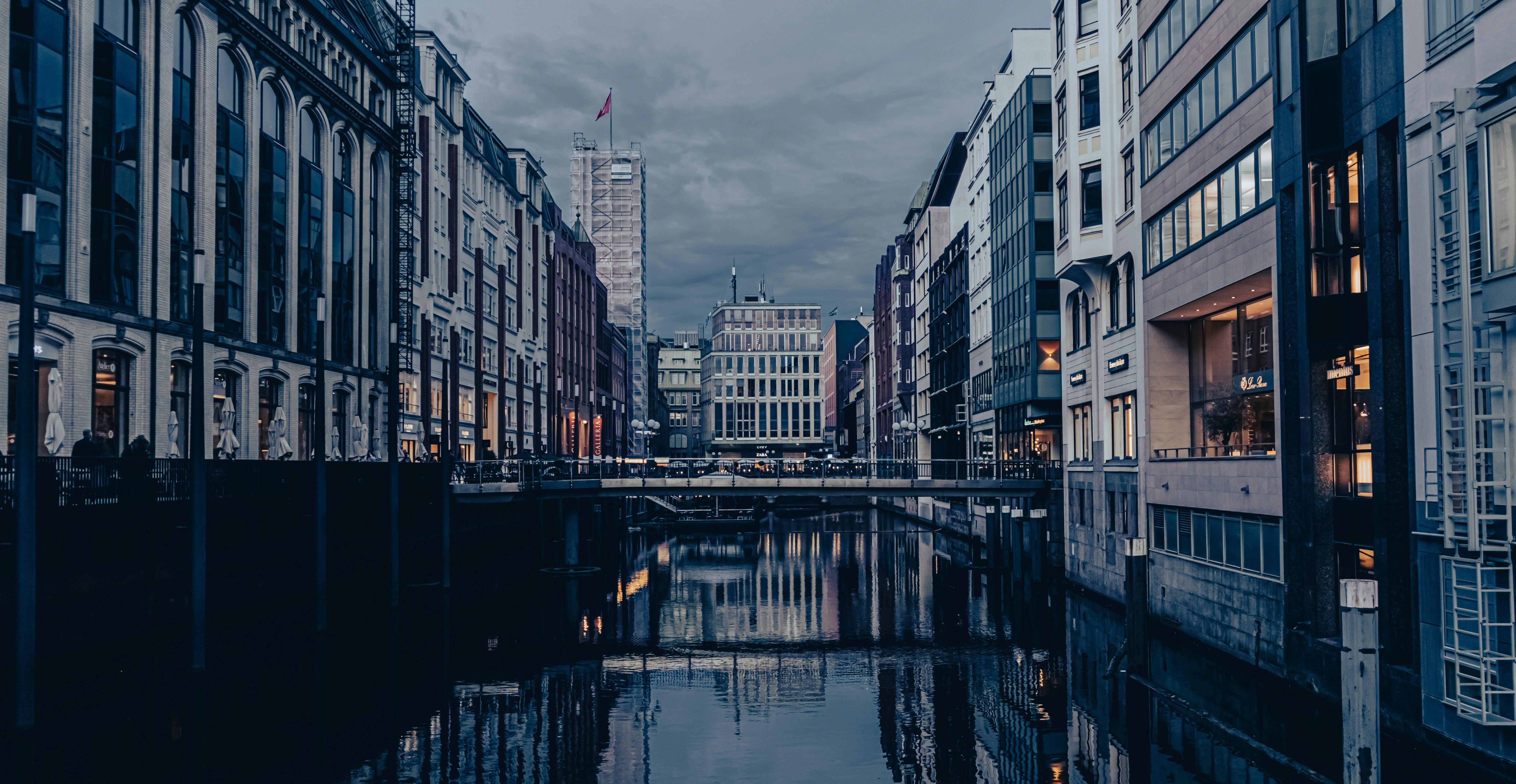 бесплатная Панорамный вид на канал, окруженный городской архитектурой, в сумерках, демонстрирующий прекрасные отражения. Стоковое фото