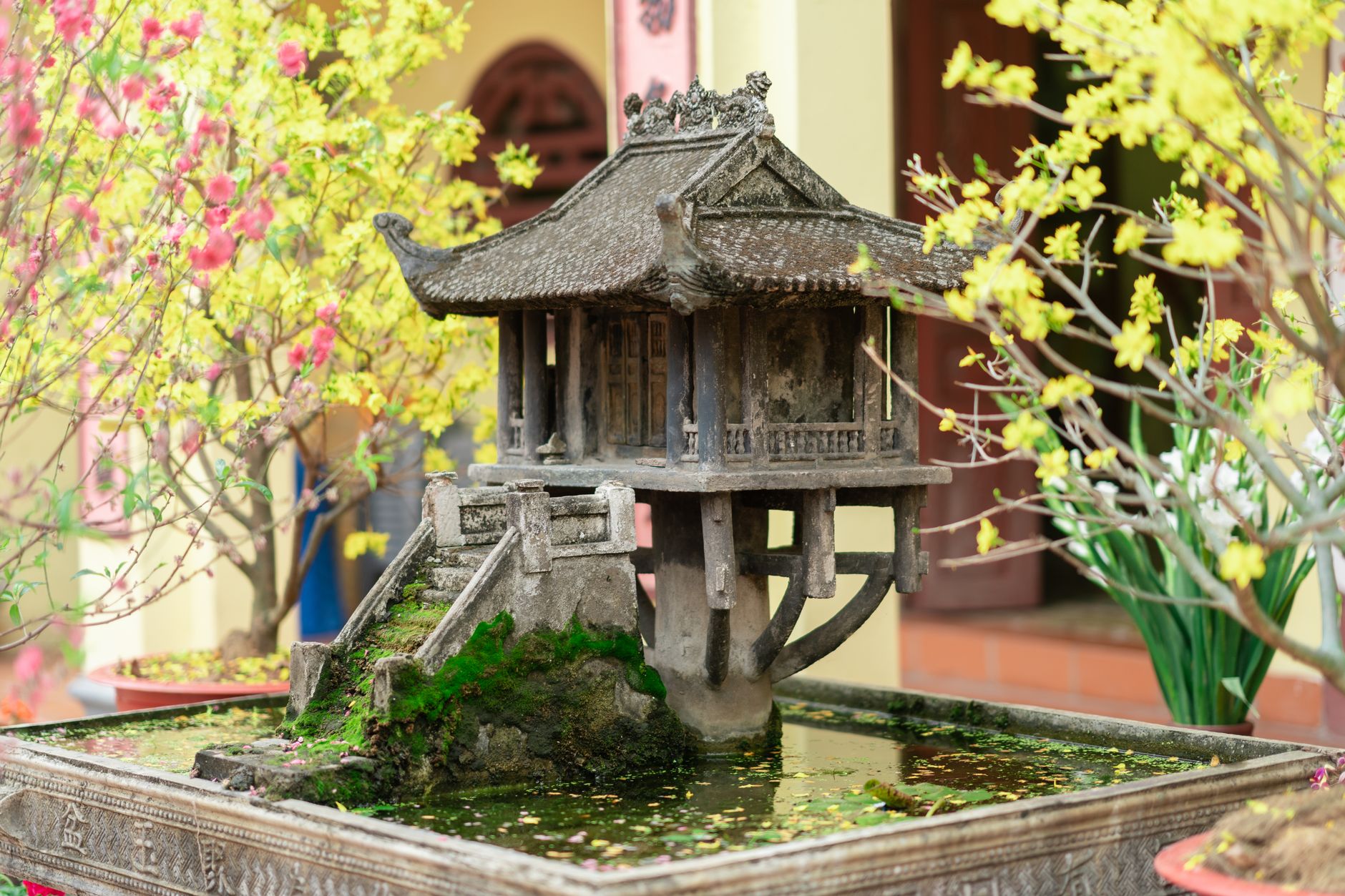 A detailed miniature of the One Pillar Pagoda surrounded by colorful blossoms and lush greenery.
