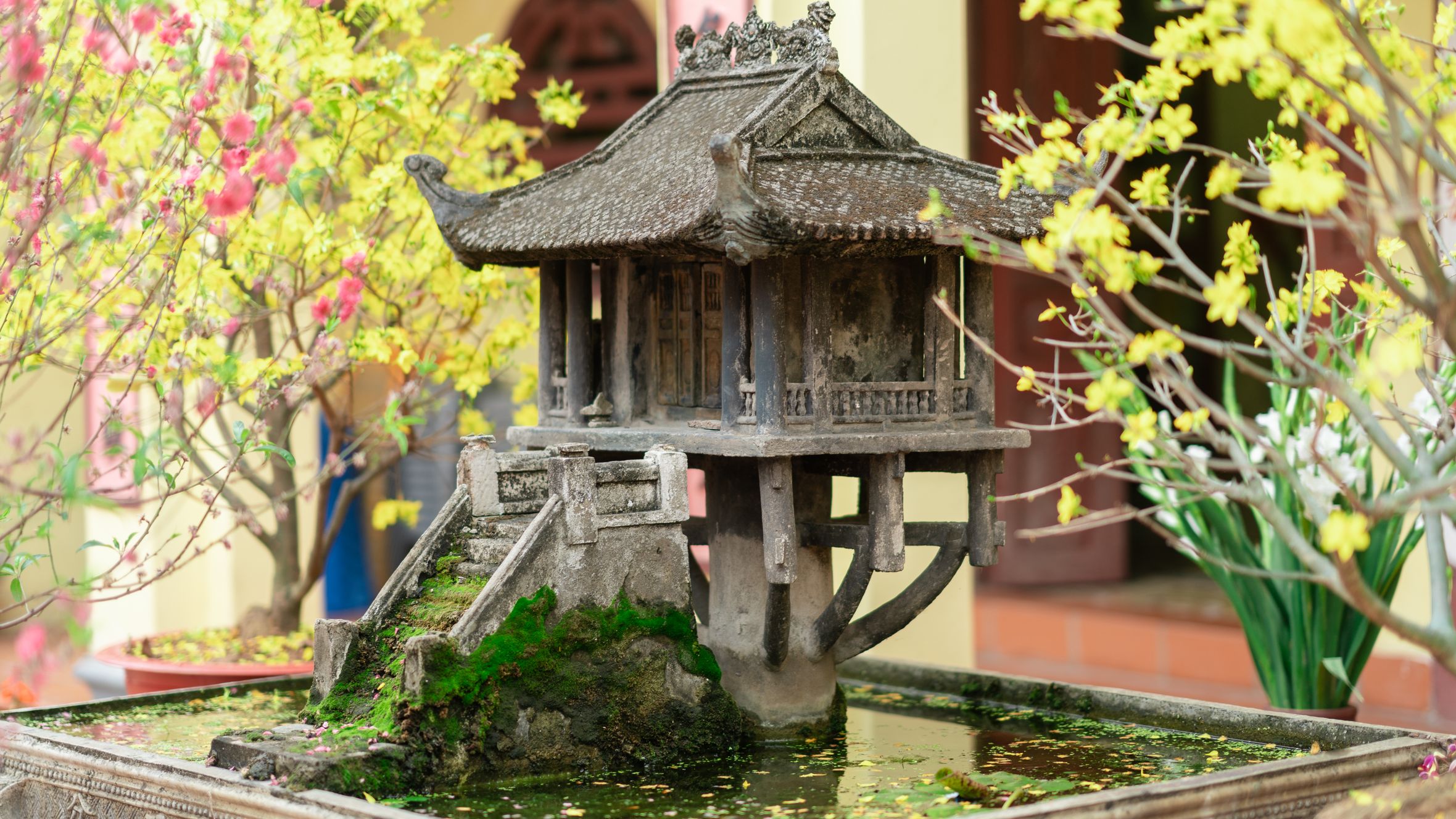 A detailed miniature of the One Pillar Pagoda surrounded by colorful blossoms and lush greenery.